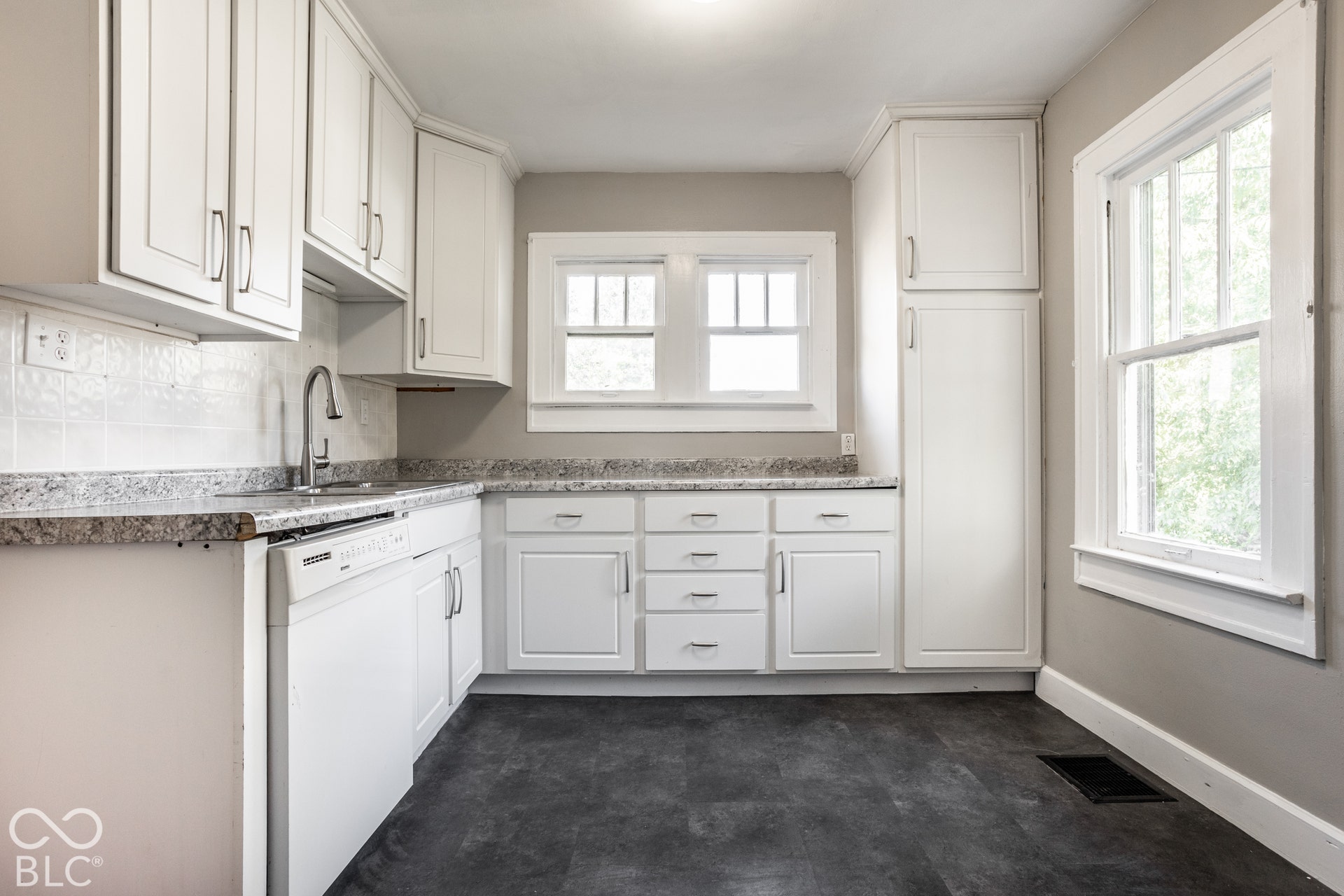 White cabinetry with brushed nickel hardware, light-toned countertops, white tile backsplash, and a stainless steel sink with a gooseneck faucet