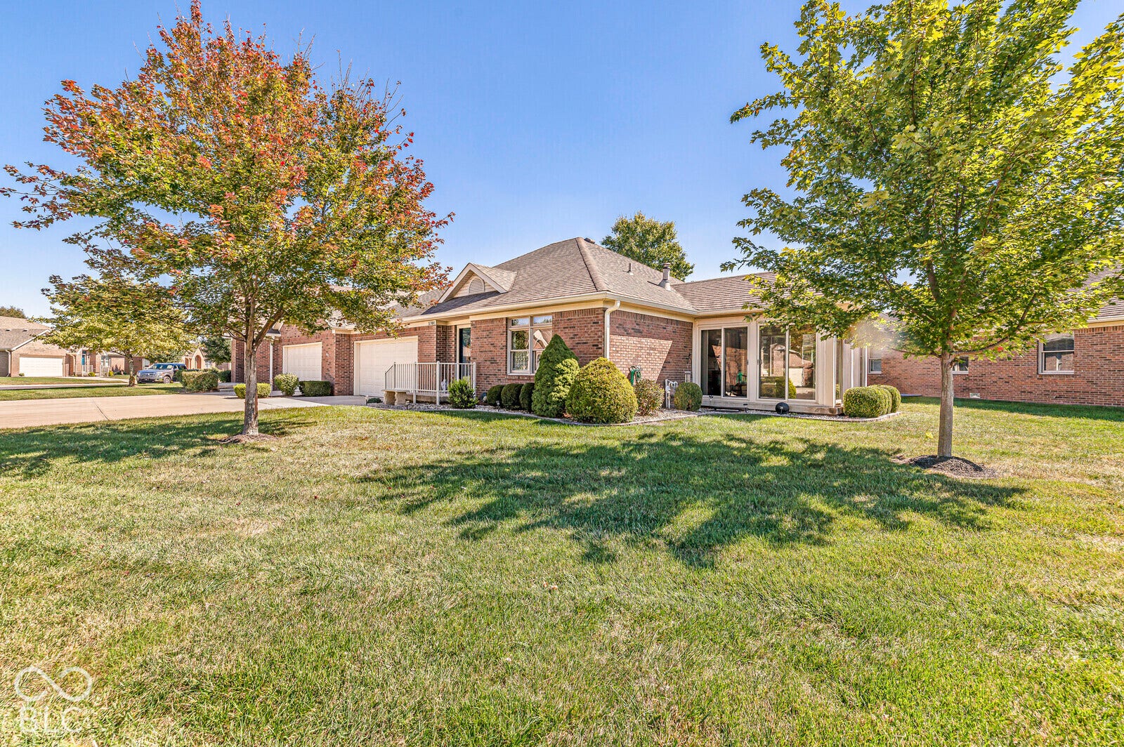 Brick exterior with an attached garage, mature trees, and a sunroom with large windows