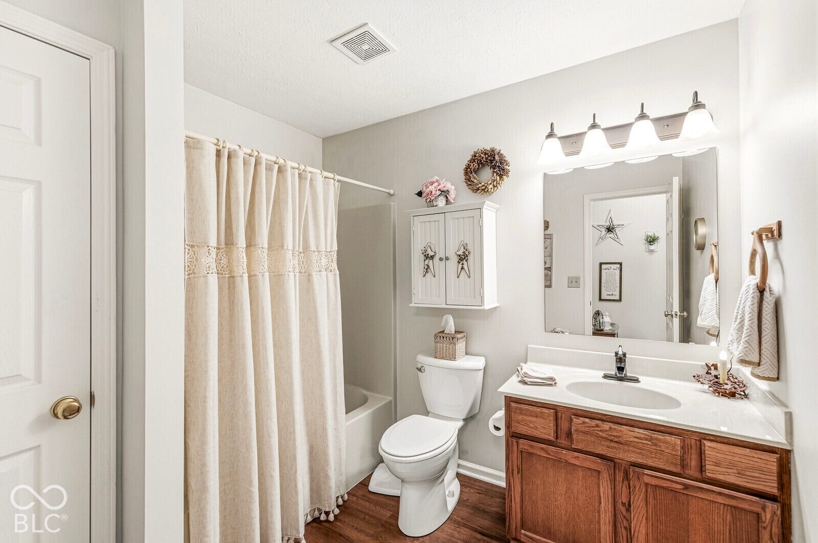 Wood-finish flooring, built-in vanity with white countertop, integrated sink, mirrored wall, and overhead lighting fixture
