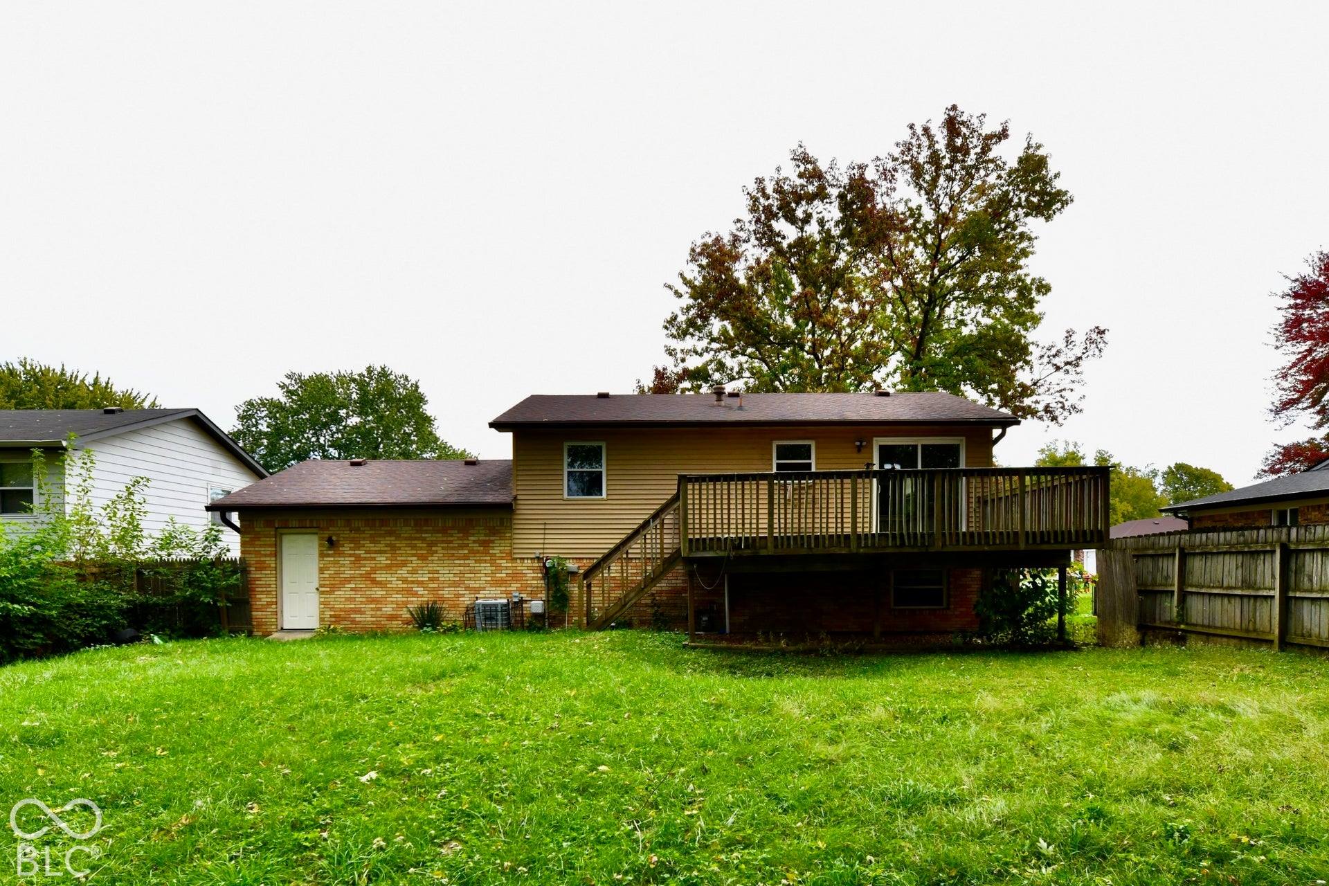 Expansive green lawn, wood deck with railing, sliding glass door, brick facade, and wood-paneled siding