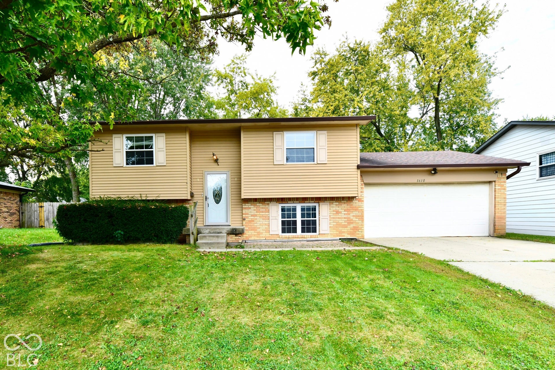 Beige siding exterior with brick accents, attached garage, concrete driveway, and front entry with a decorative glass door