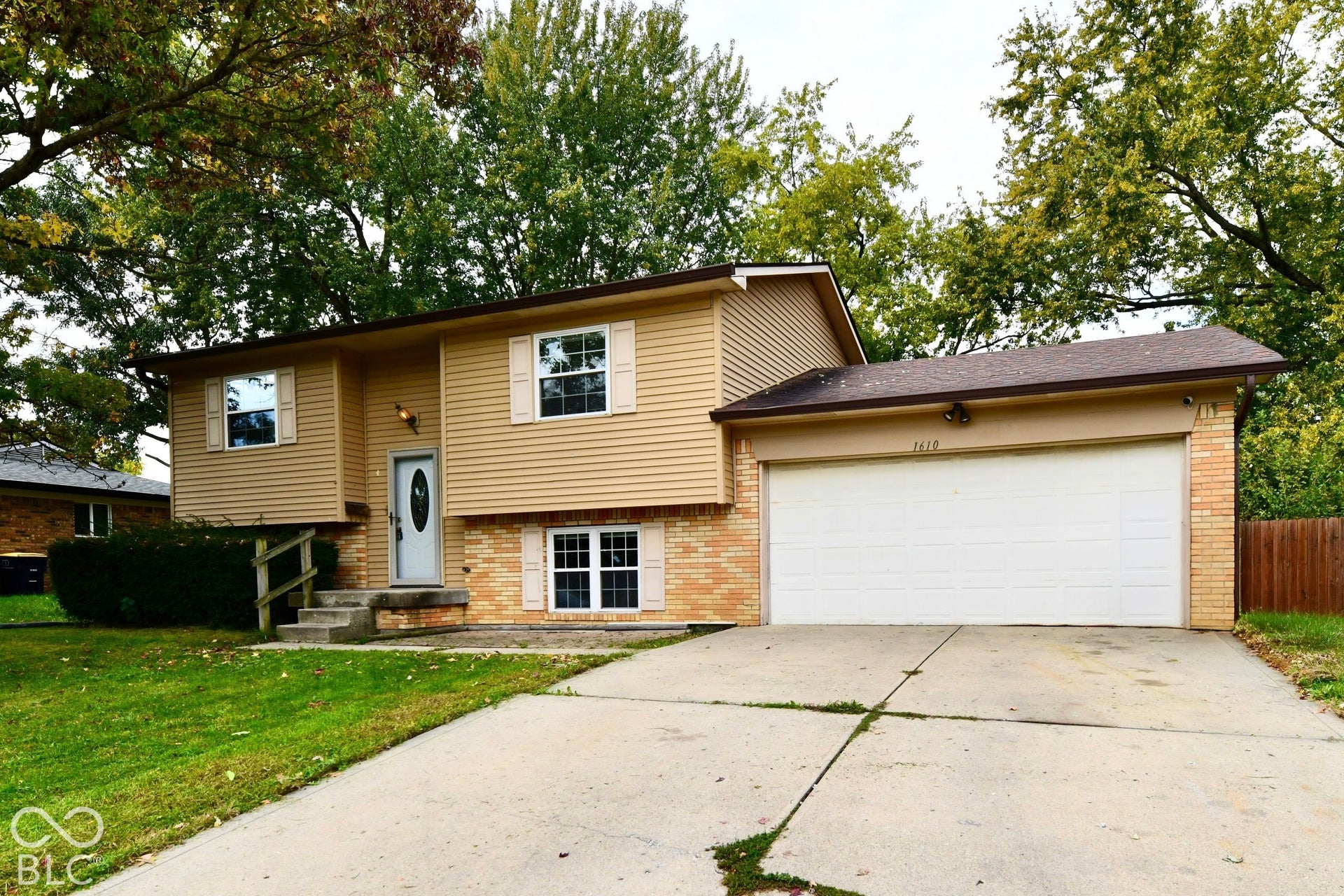 Split-level residence featuring brick and siding exterior, an attached garage, a concrete driveway, and a front entry with a white door
