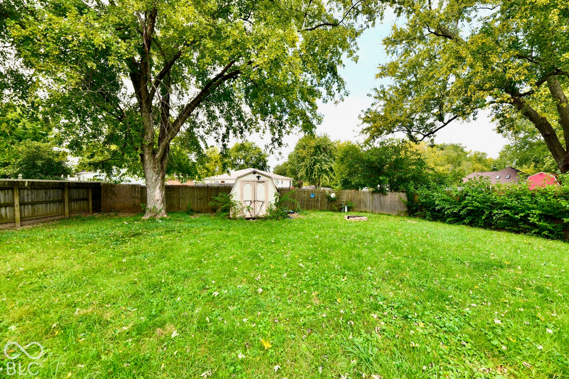Spacious lawn area, mature trees, wood fence enclosure, and storage shed
