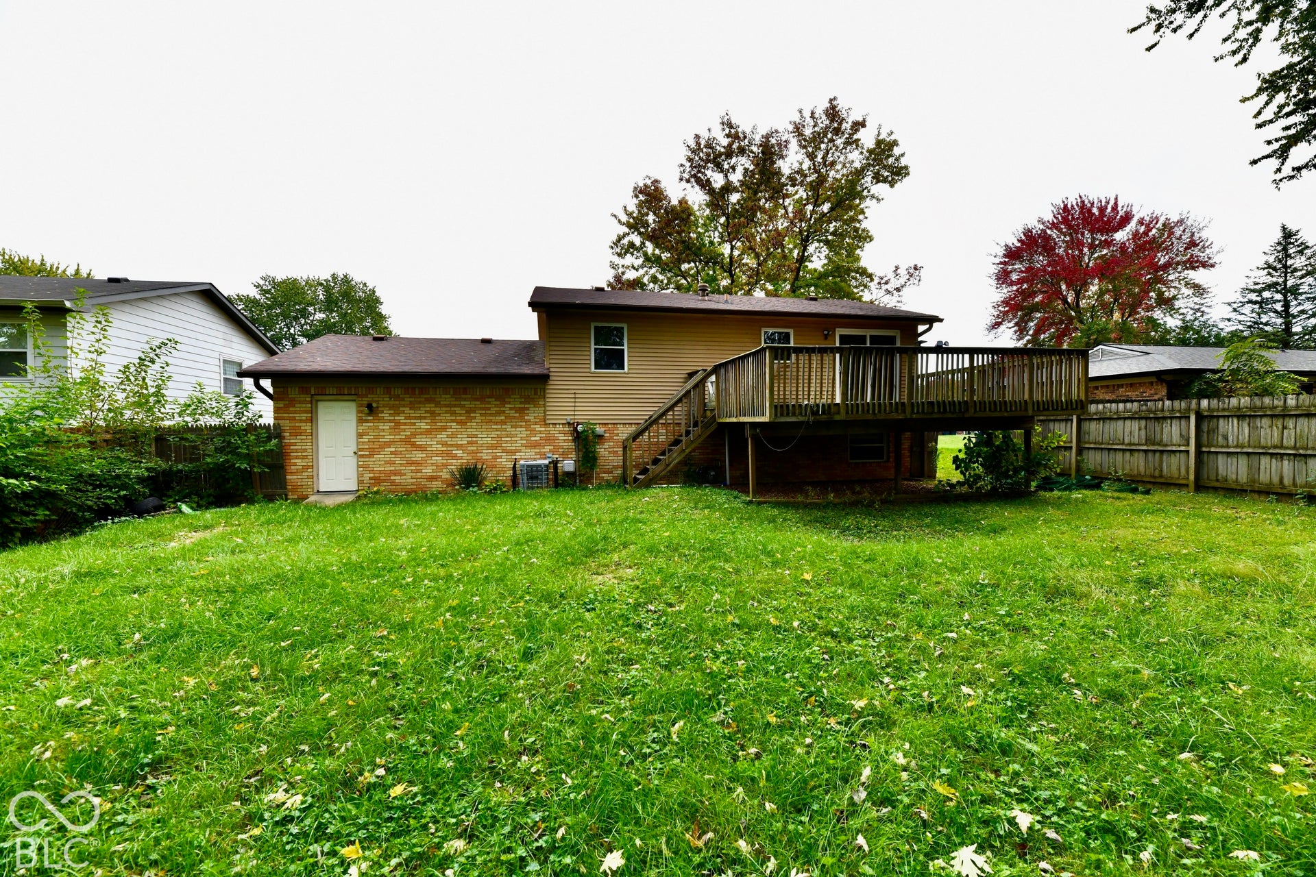Expansive green space featuring a wood deck, wood privacy fence, and brick and siding exterior