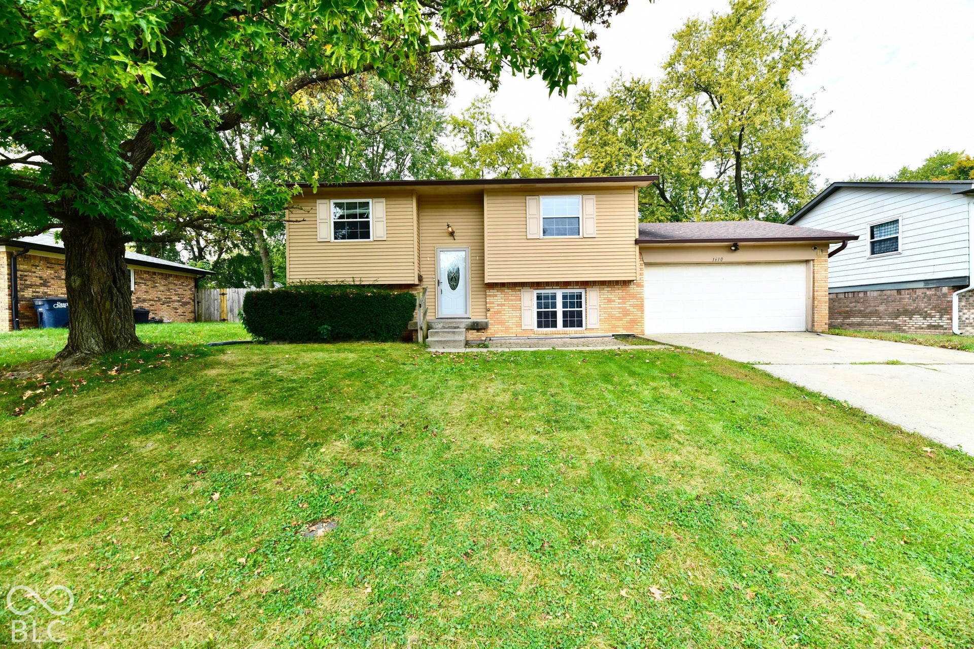 Split-level residence featuring a two-car garage, front entry steps, and a sloped lawn