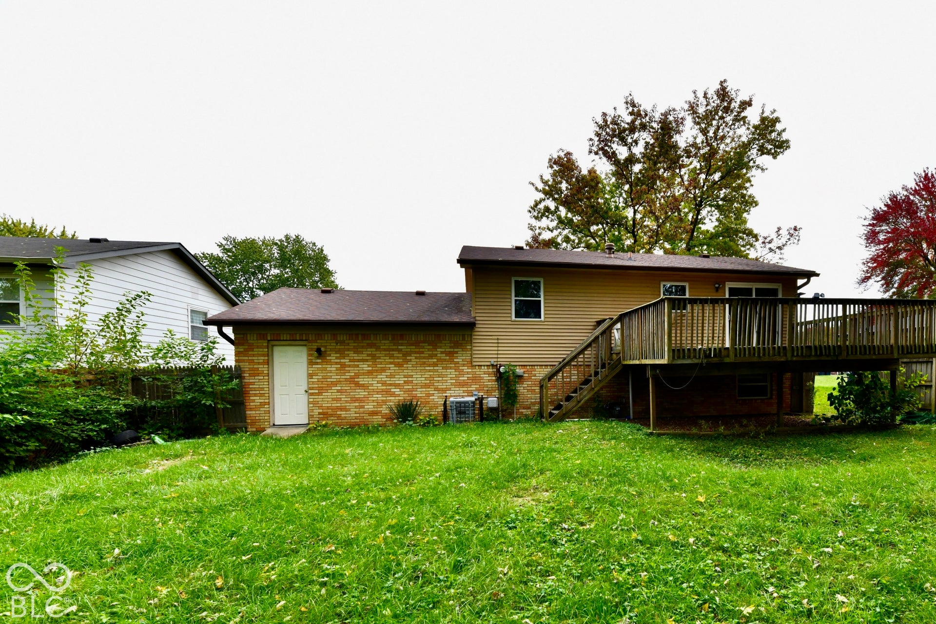 Expansive backyard featuring a large wooden deck with stairs, a brick and siding exterior, and a secondary exterior door