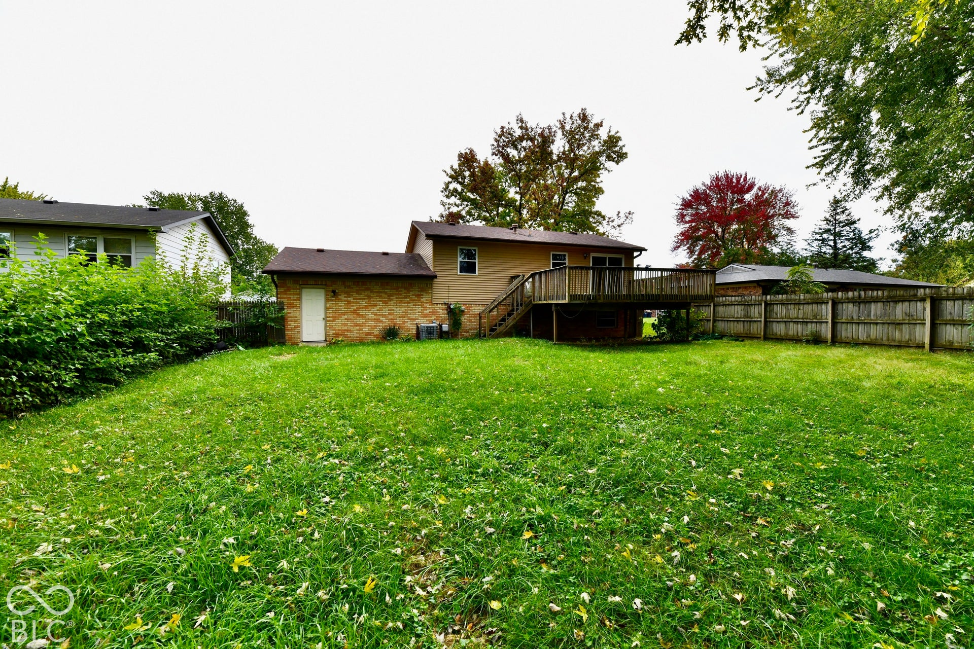Expansive green space featuring a wood deck, wood privacy fence, and brick-sided outbuilding