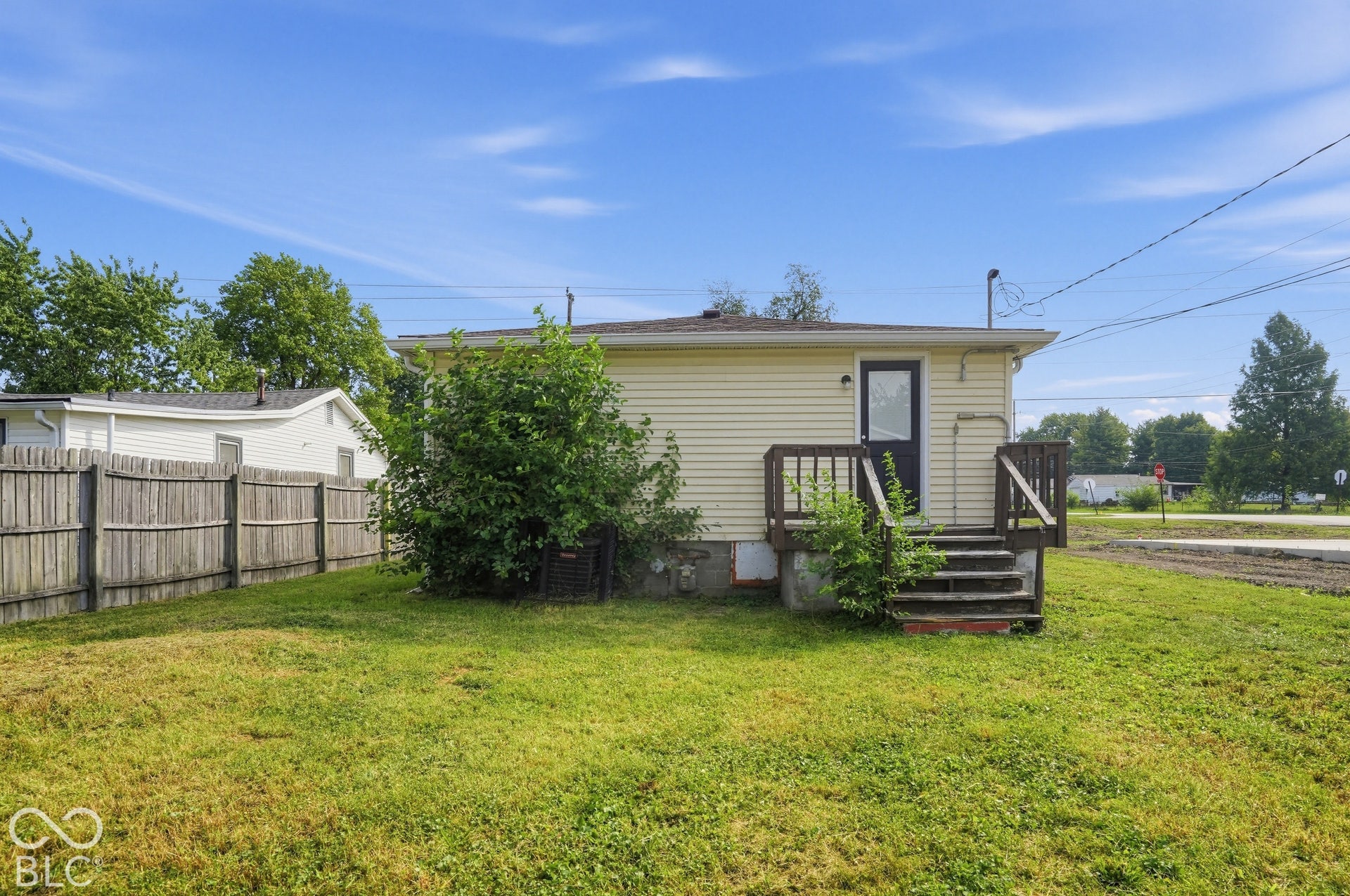 3128 S Rural Street, Indianapolis, IN 46237 Rear exterior featuring horizontal siding, a wood deck with stairs, a dark-framed entry door, and a partially fenced yard
