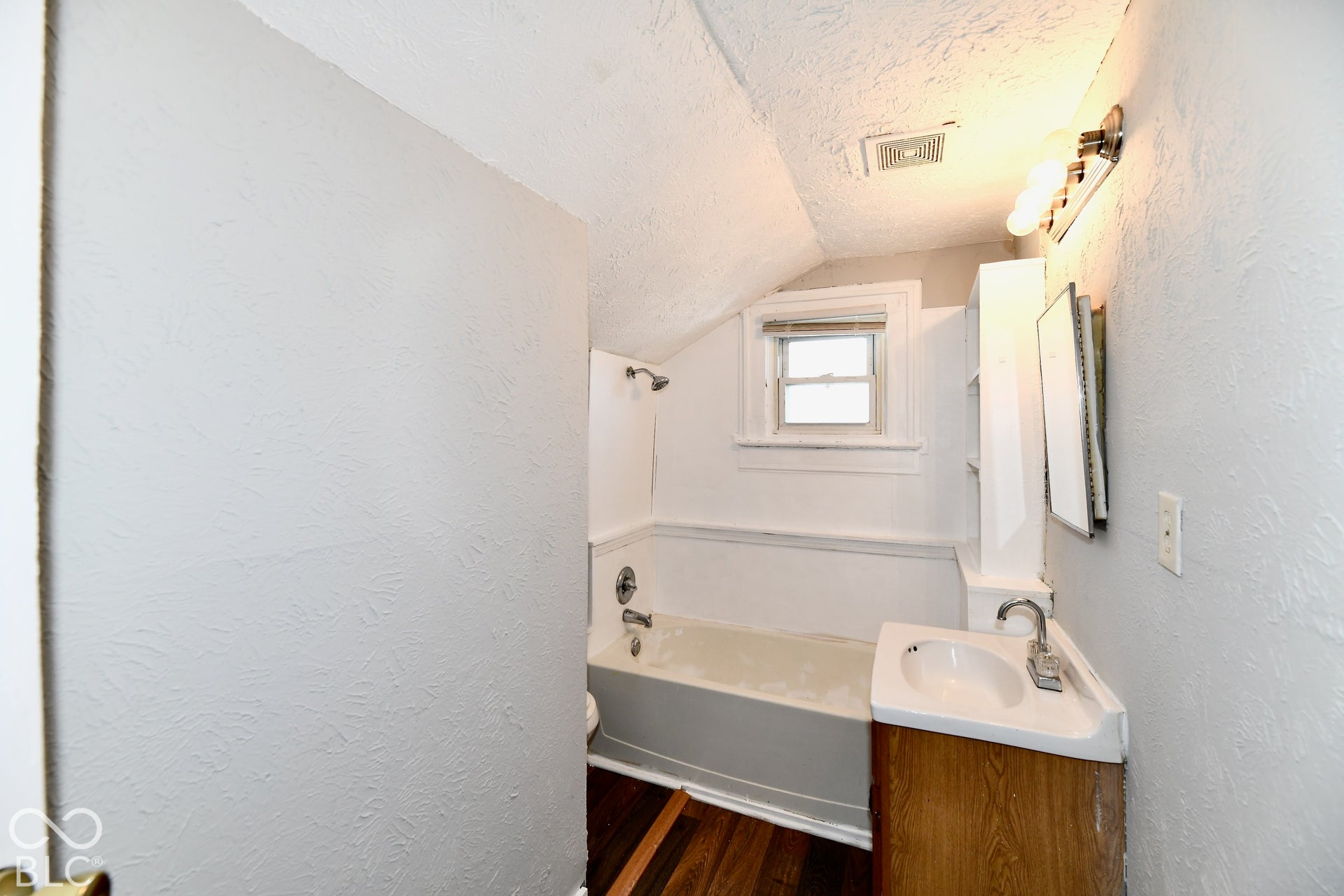 Compact bathroom featuring a corner vanity with integrated sink, wood-finish flooring, and a bathtub with an overhead shower