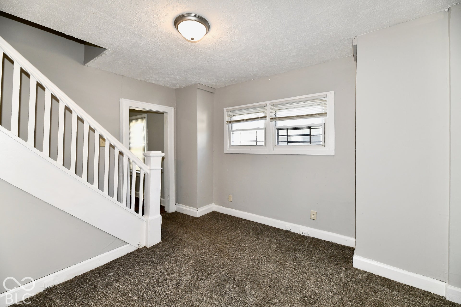 Textured carpet flooring, white painted staircase with wood balusters, light gray wall finish, and flush-mount ceiling lighting