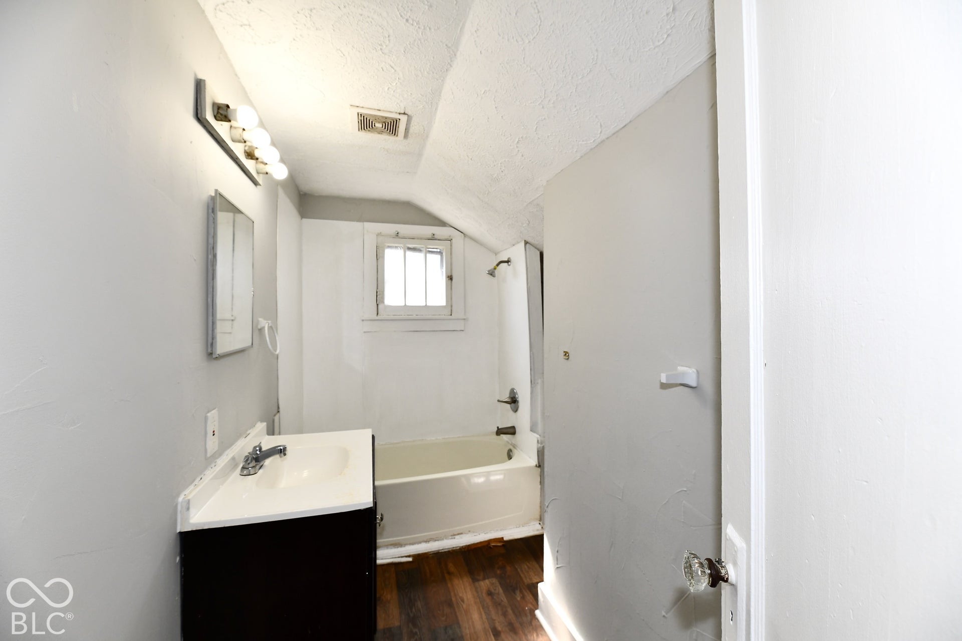 Bathroom featuring a single vanity, built-in bathtub, and wood-finish flooring