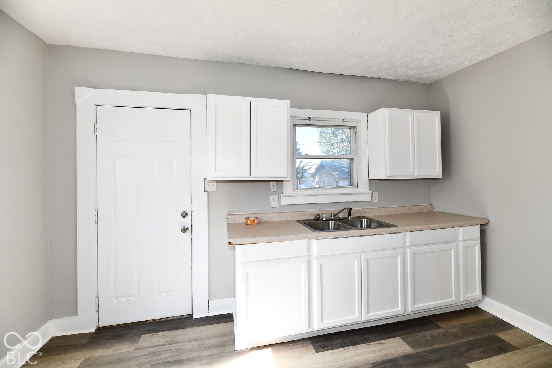 White cabinetry with brushed nickel hardware, dual-basin stainless steel sink, light-toned countertop, and wood-finish flooring