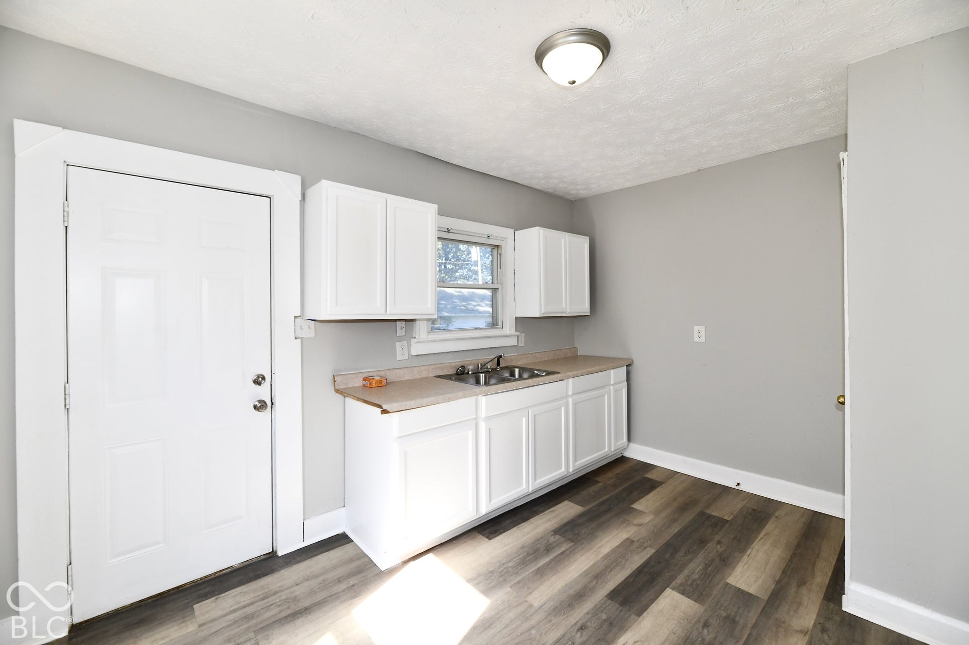 White shaker-style cabinetry, double basin sink, neutral countertops, wood-finish flooring, and a flush mount ceiling light fixture