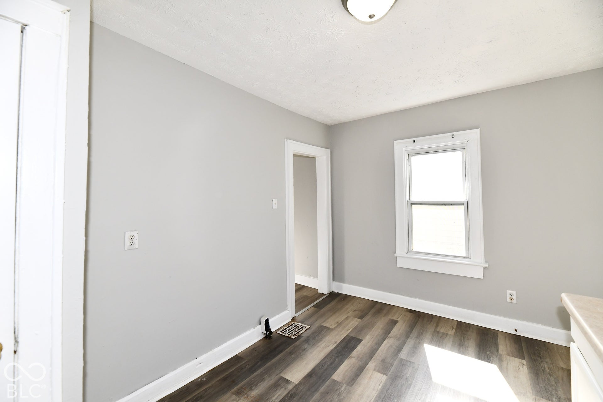Wood-finish flooring, light gray walls, white trim, recessed lighting, and a single window
