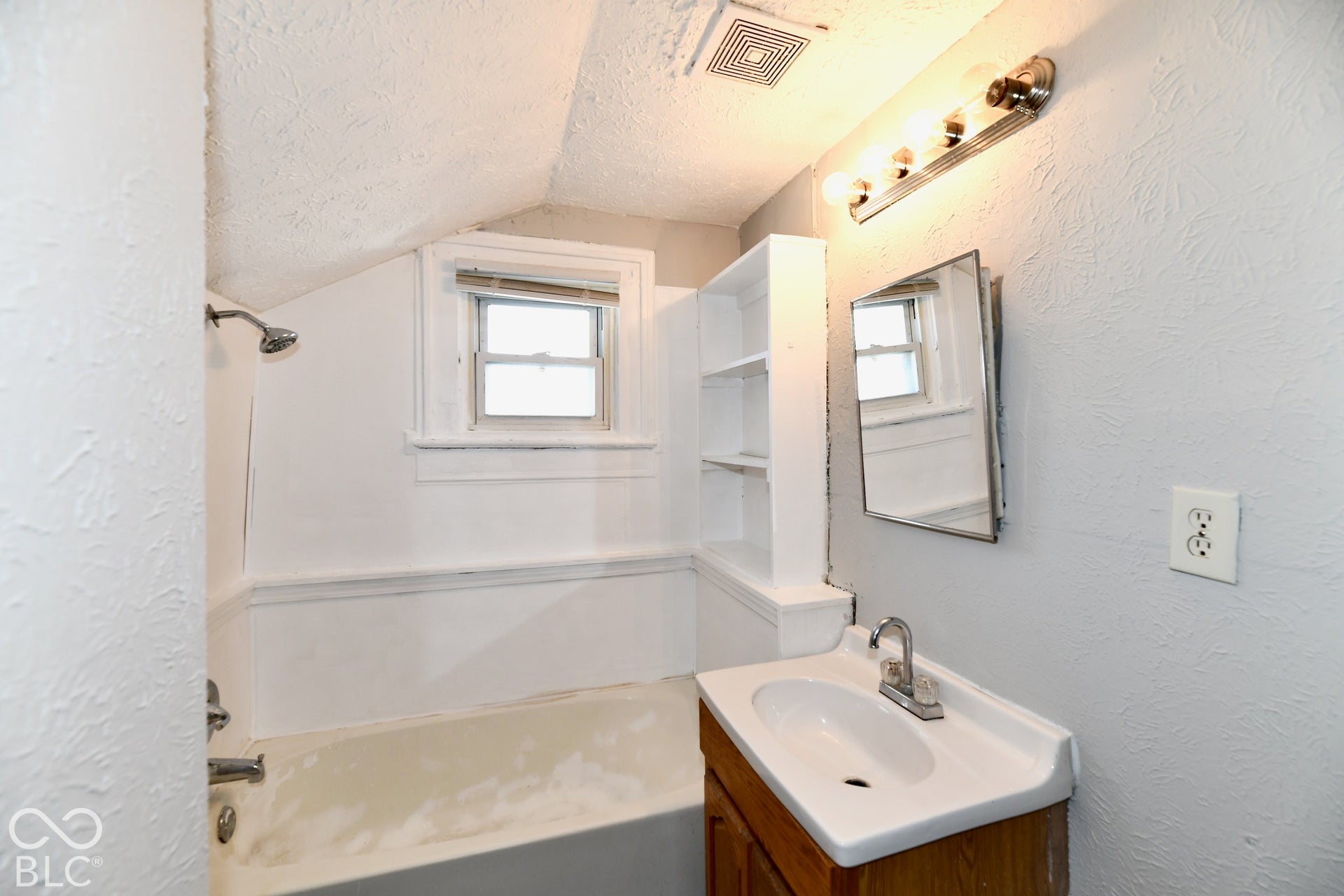 Built-in shelving, vanity with integrated sink, wall-mounted mirror, and tub with shower fixture