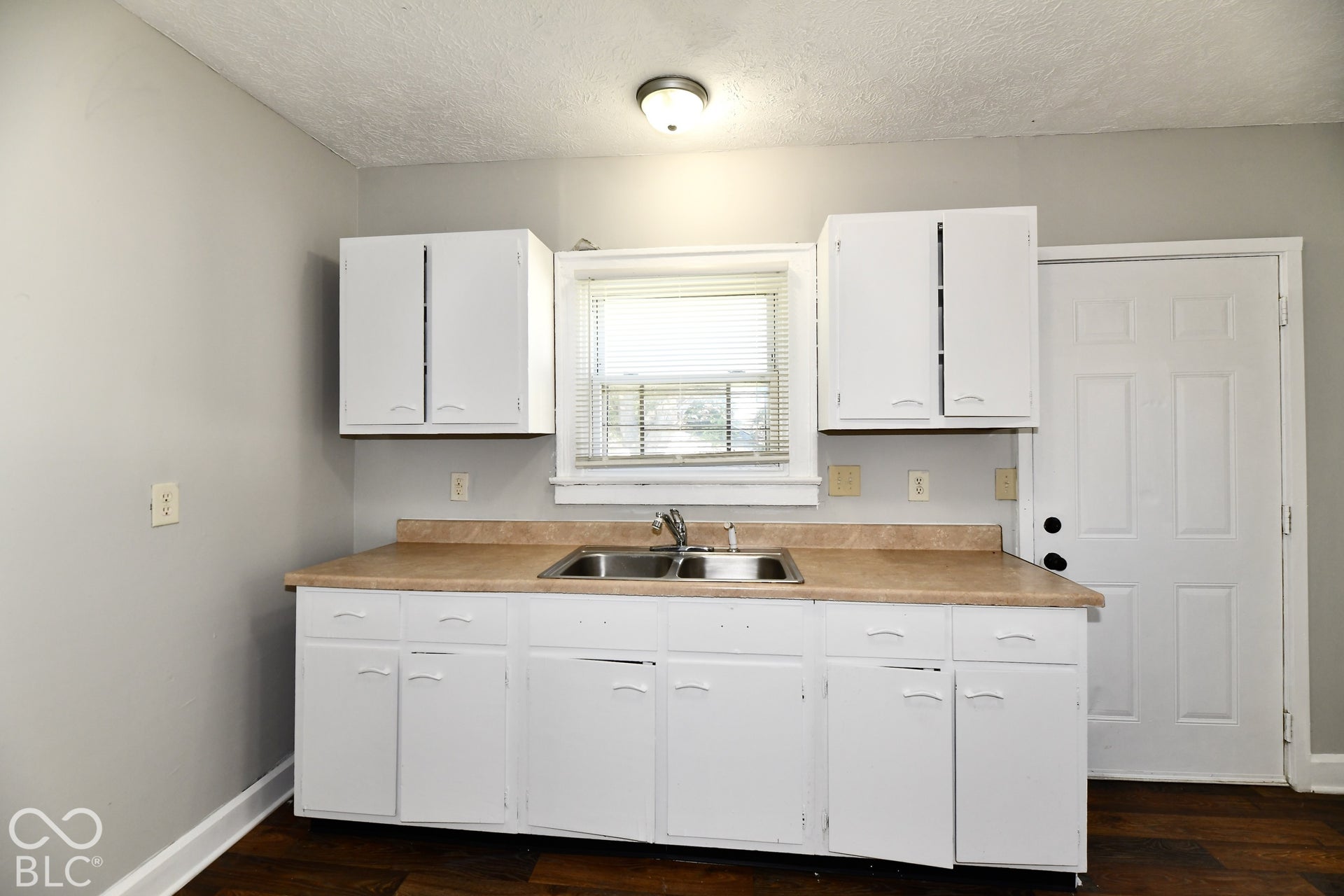 White cabinetry with curved pulls, stainless steel double basin sink, light-toned countertop, wood-finish flooring, and a panel door
