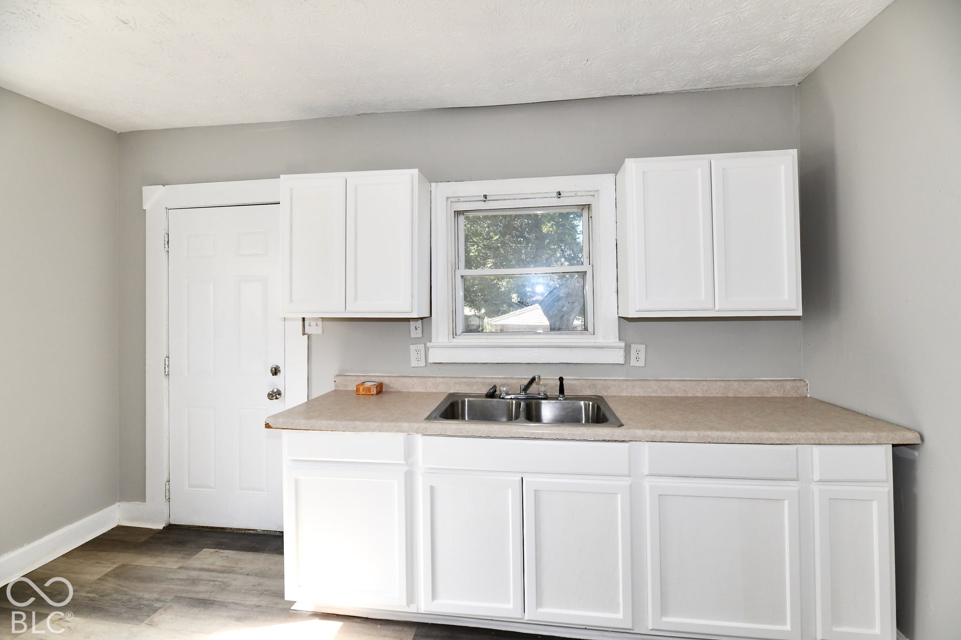 White cabinetry with a double basin sink, light-toned countertop, and wood-finish flooring