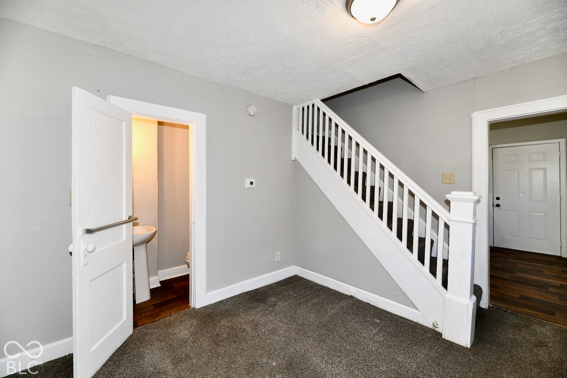 Carpeted flooring, painted walls, white trim, white staircase with balusters, and a light fixture