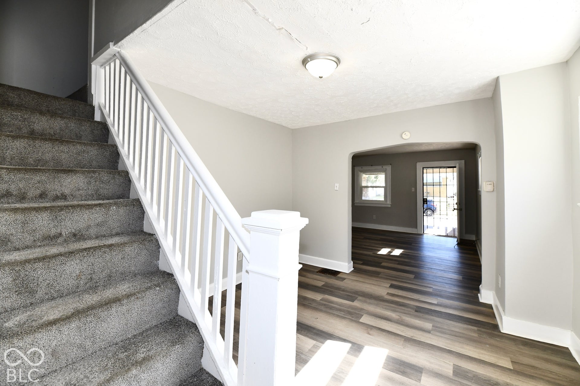 Carpeted staircase with white railing, wood-finish flooring, light gray wall paint, and an arched doorway