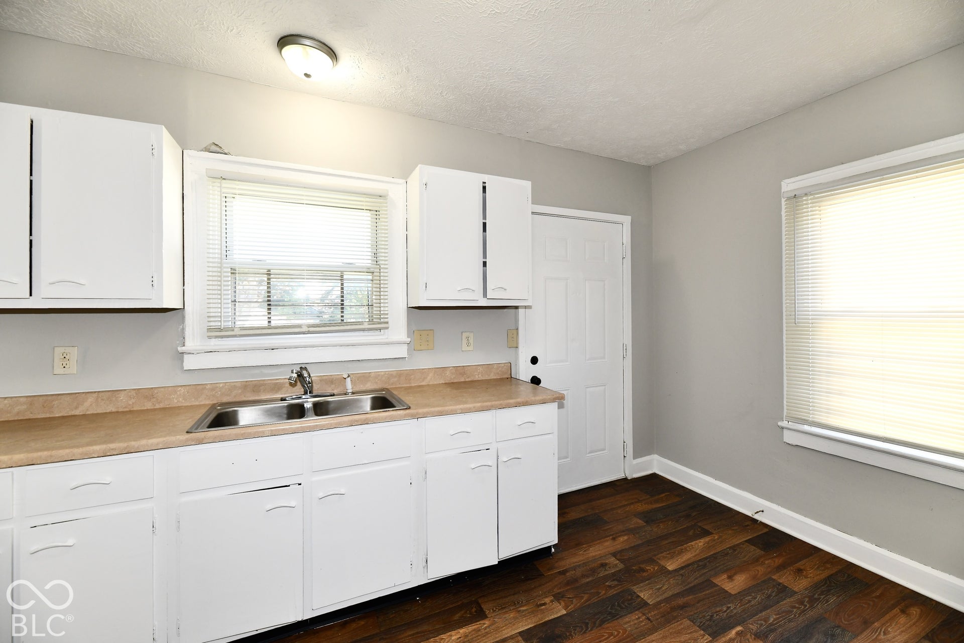 Kitchen featuring white cabinetry, a dual basin stainless steel sink, wood-finish flooring, and a window with blinds