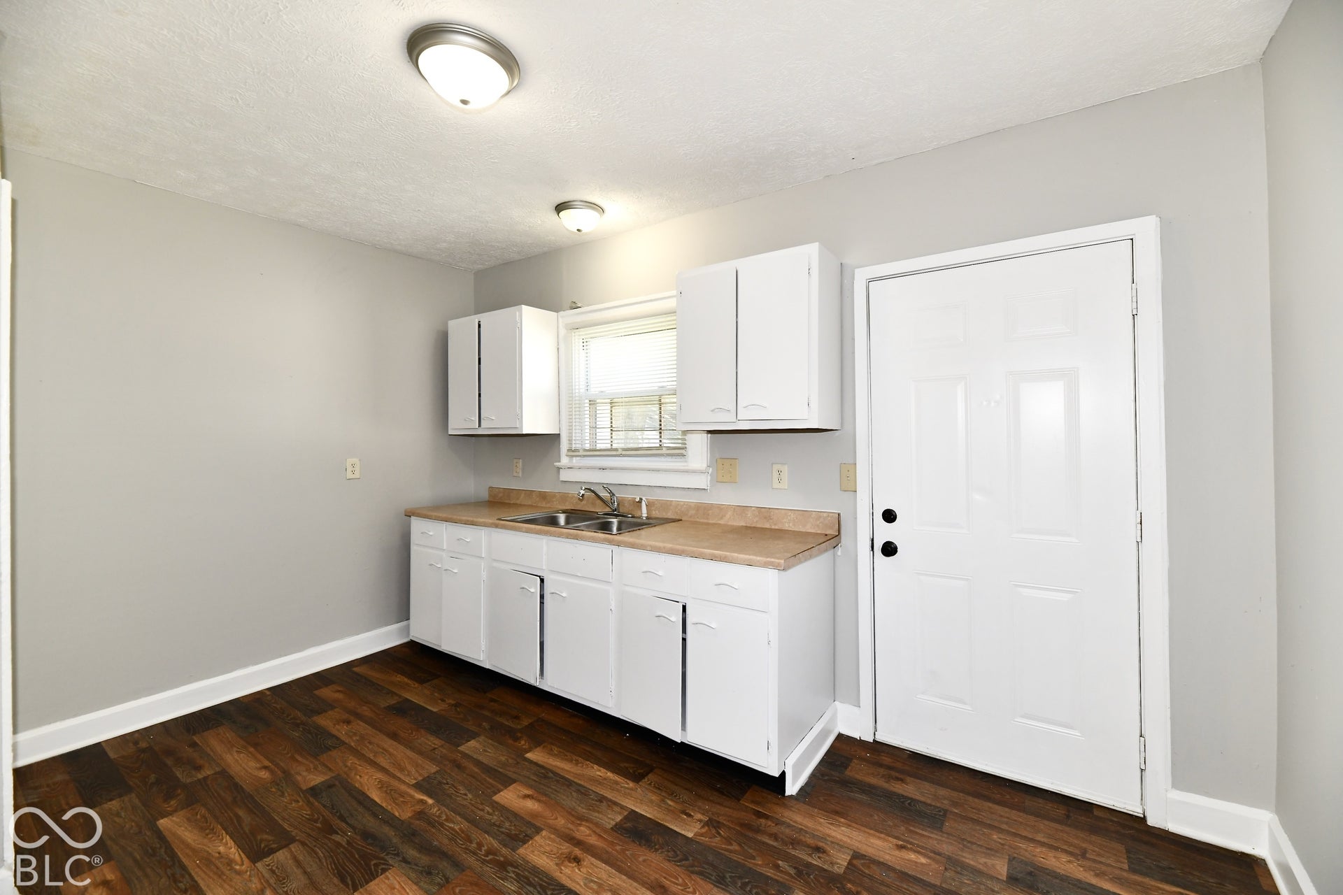 Kitchen area featuring wood-finish flooring, white cabinetry, a double basin sink, and neutral wall paint