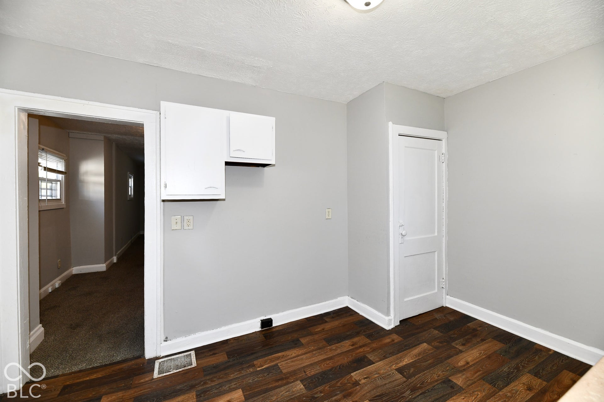 Wood-finish flooring with white trim, light gray painted walls, and white upper cabinetry