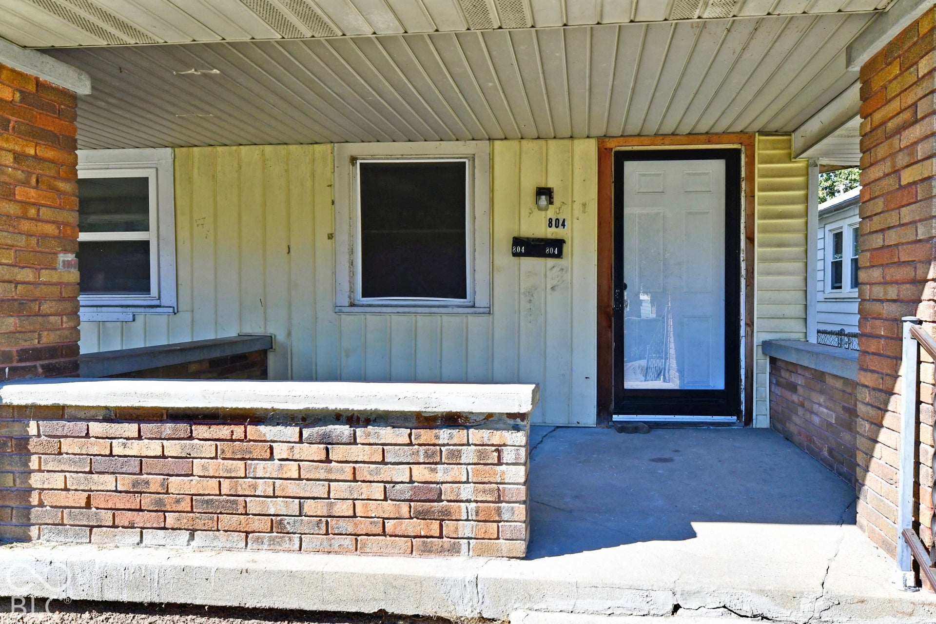Covered front porch featuring brick pilasters and concrete flooring