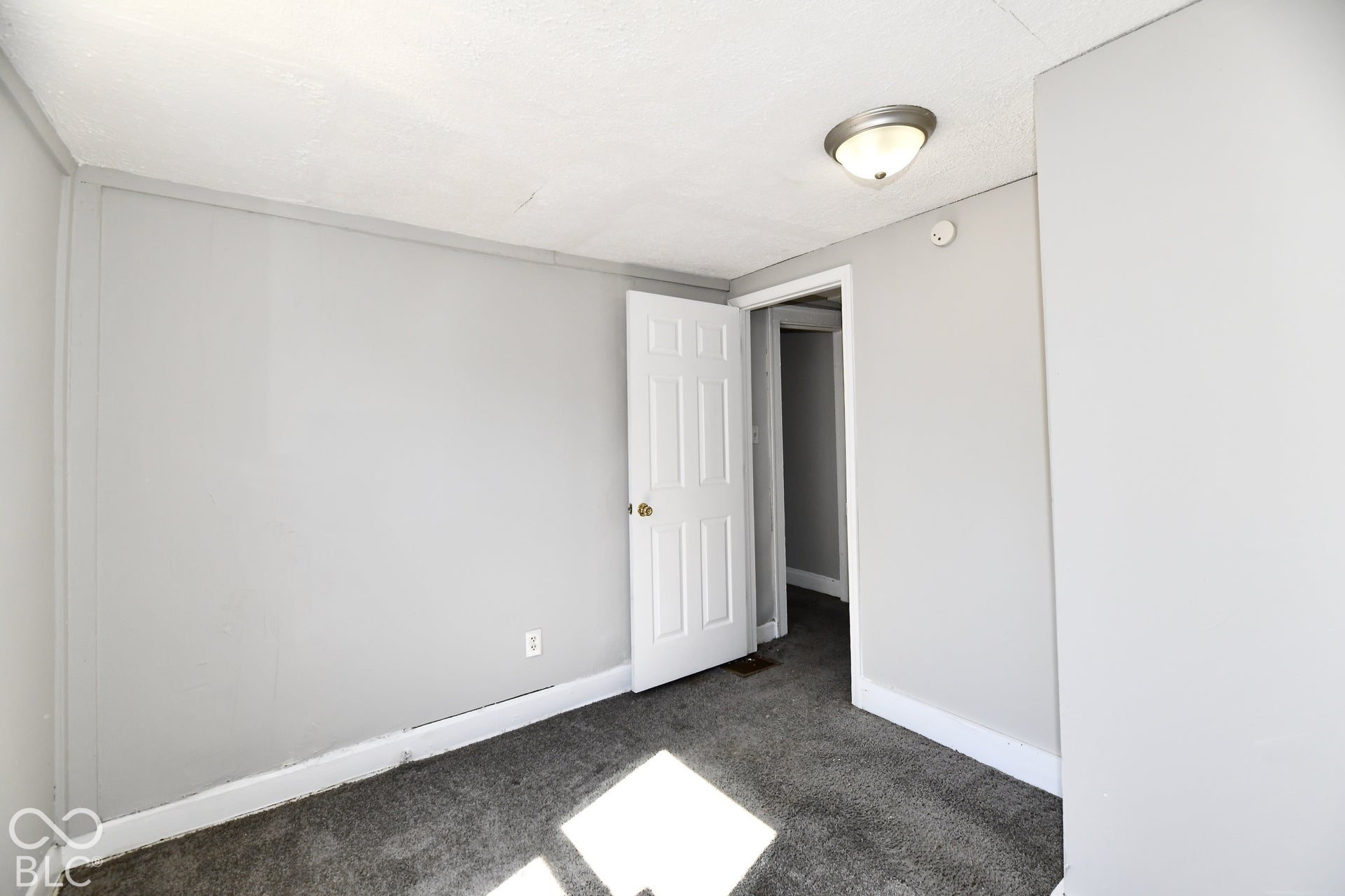 Neutral gray wall paint, textured ceiling, flush mount ceiling light fixture, white interior door, dark gray carpet flooring