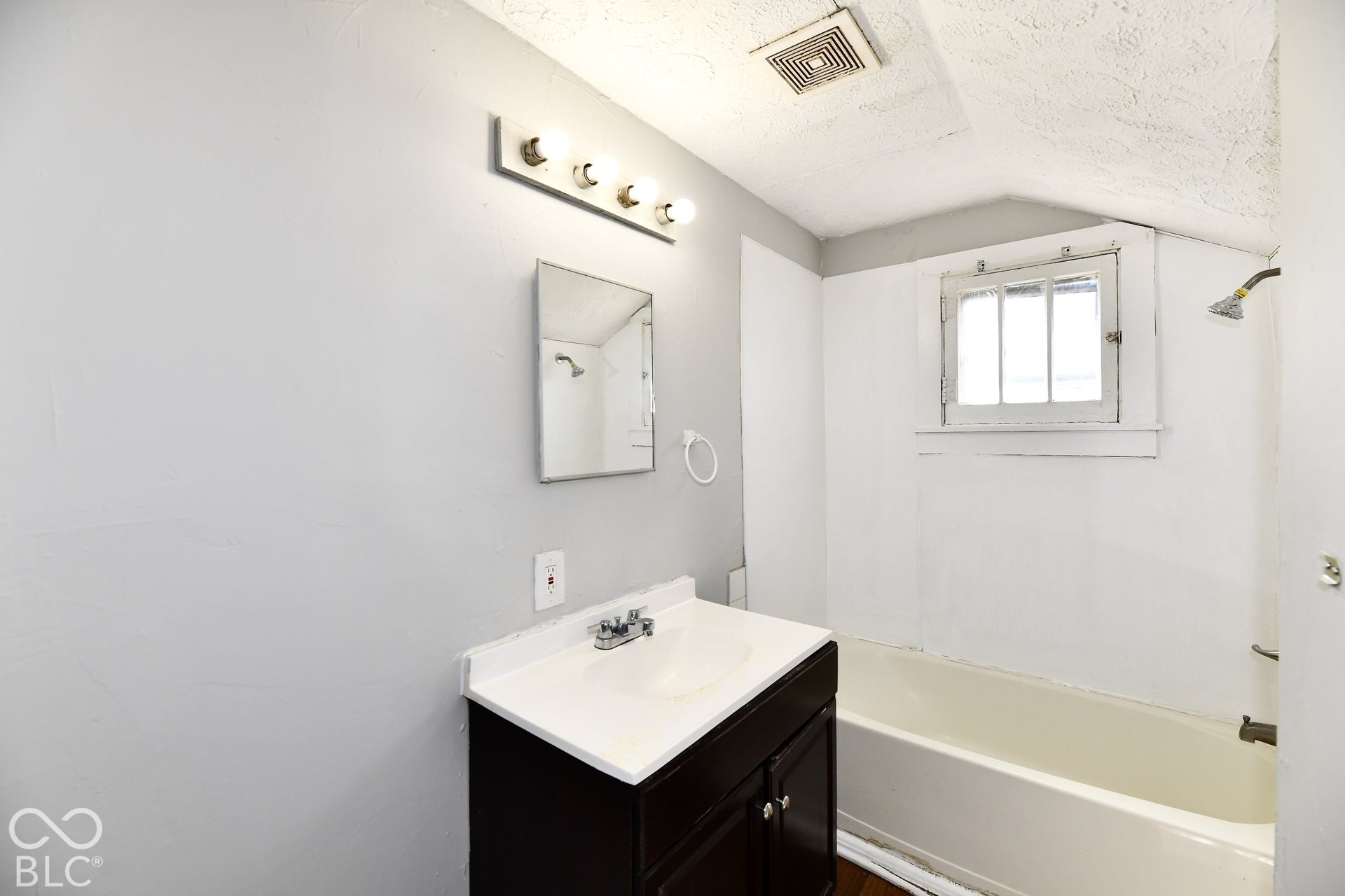Bathroom featuring a dark wood-finish vanity with a white countertop and integrated sink, a rectangular mirror, and a wall-mounted light fixture with four bulbs