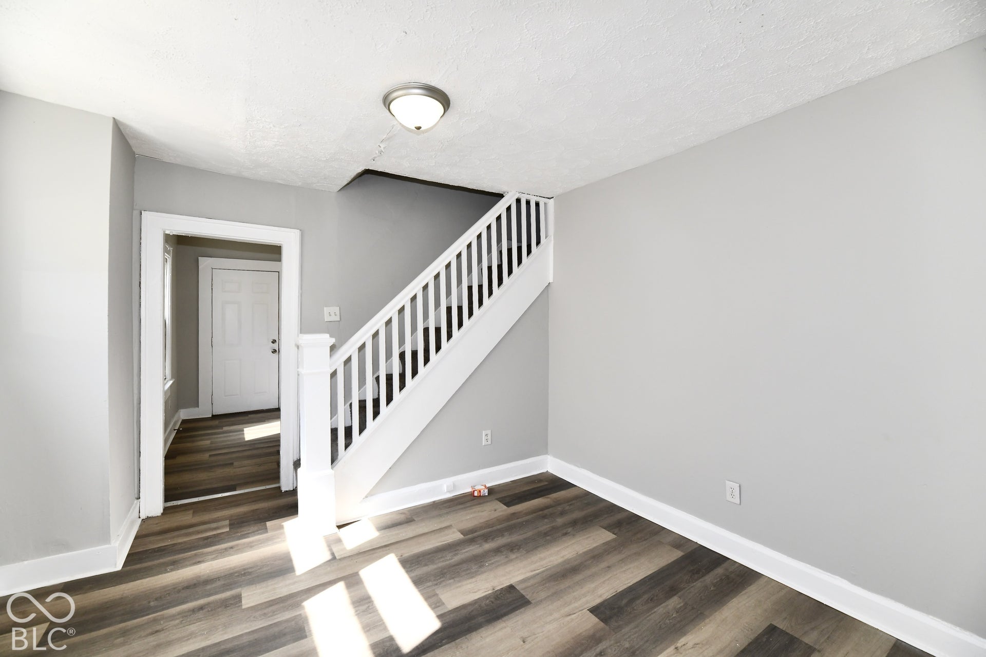 Wood-finish flooring with light gray wall paint, white trim, a white staircase, and a flush-mount ceiling light fixture