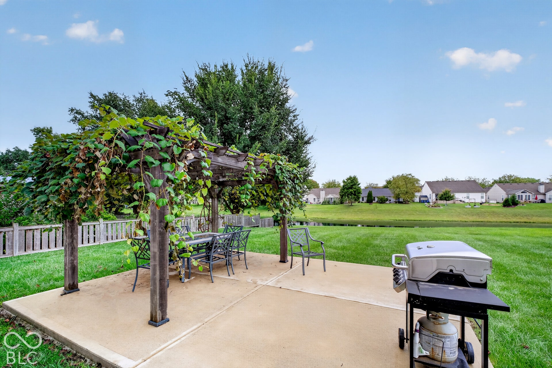 15996 Arbor Grove Boulevard, Noblesville, IN 46060 Concrete patio featuring a wood pergola with mature climbing vines, expansive grassy area, and a body of water in the background
