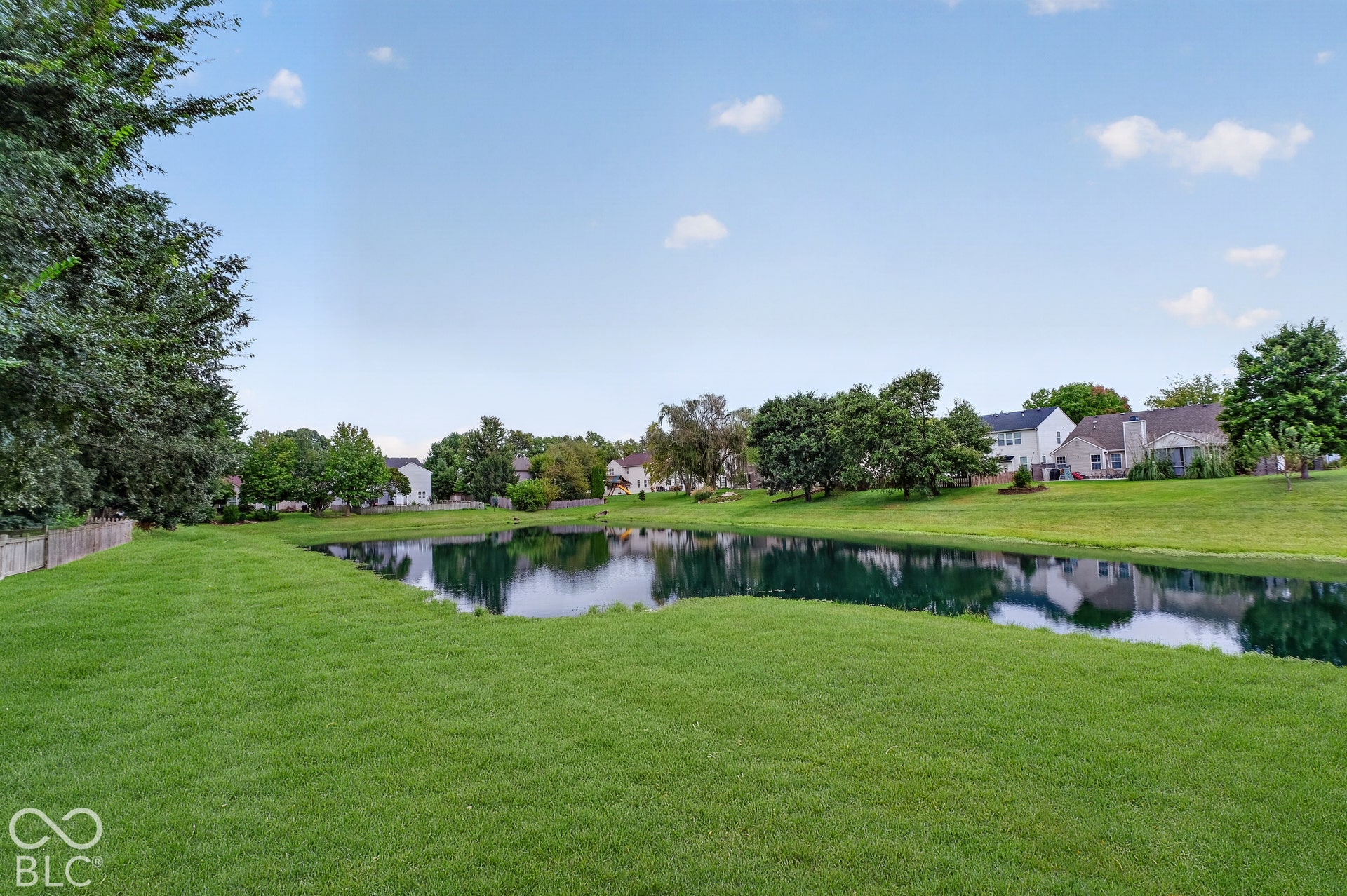 15996 Arbor Grove Boulevard, Noblesville, IN 46060 Expansive green lawn bordering a reflective pond, with mature trees and residential properties in the background
