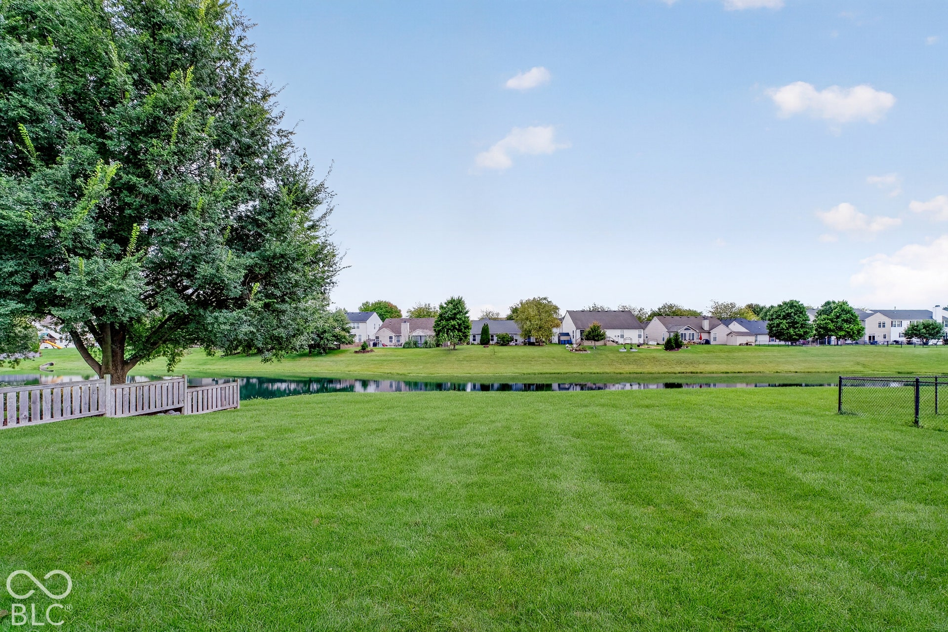 15996 Arbor Grove Boulevard, Noblesville, IN 46060 Expansive green lawn with a water feature, mature tree, and a decorative wooden fence