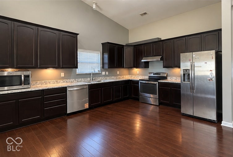 4348 Big Leaf Lane, Indianapolis, IN 46239 Vaulted ceiling with track lighting, dark wood-finish cabinetry, light-toned countertops, stainless steel appliances, and wood-finish flooring