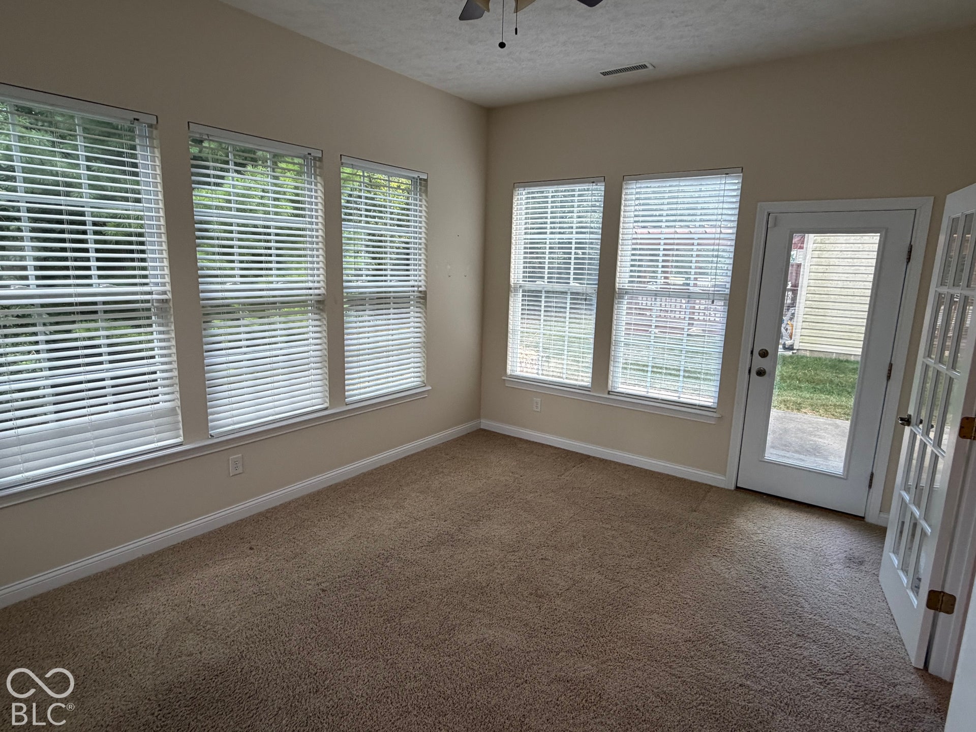 Vaulted ceiling room featuring multiple windows with blinds, a glass-paned door, and carpet flooring