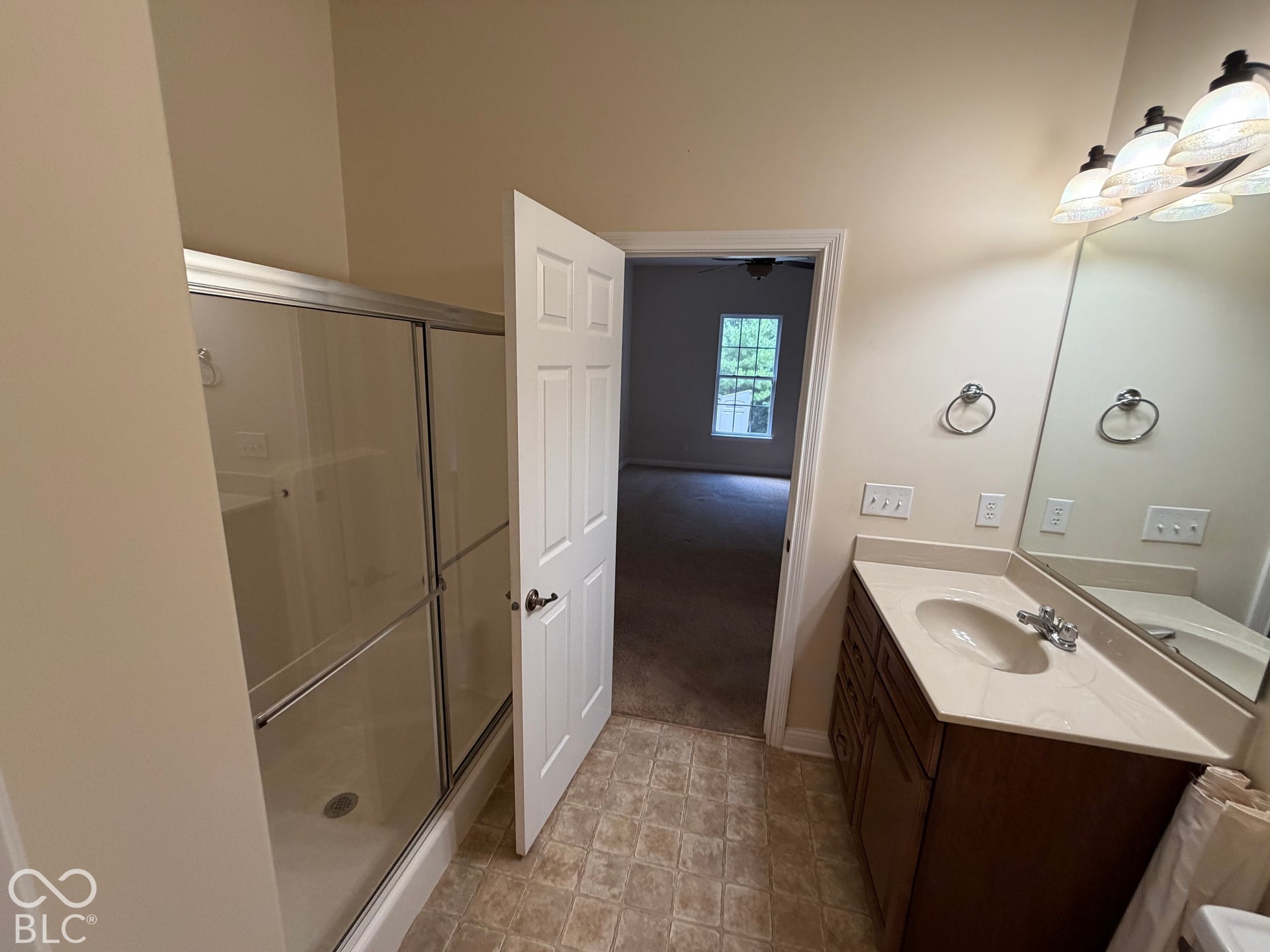 Vanity with an integrated sink and light-toned countertop, vanity mirror with a three-light fixture, and a shower with sliding glass doors