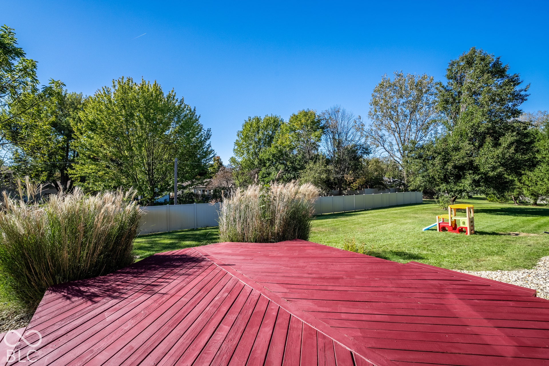 Expansive backyard featuring a red-painted wood deck, manicured lawn, and mature trees