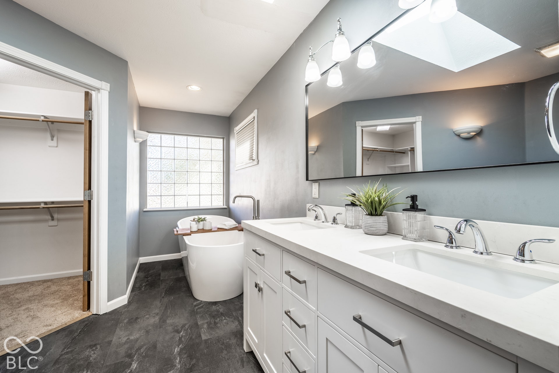 Renovated primary suite bathroom with double vanity, soaking tub, skylight, entry to walk-in closet