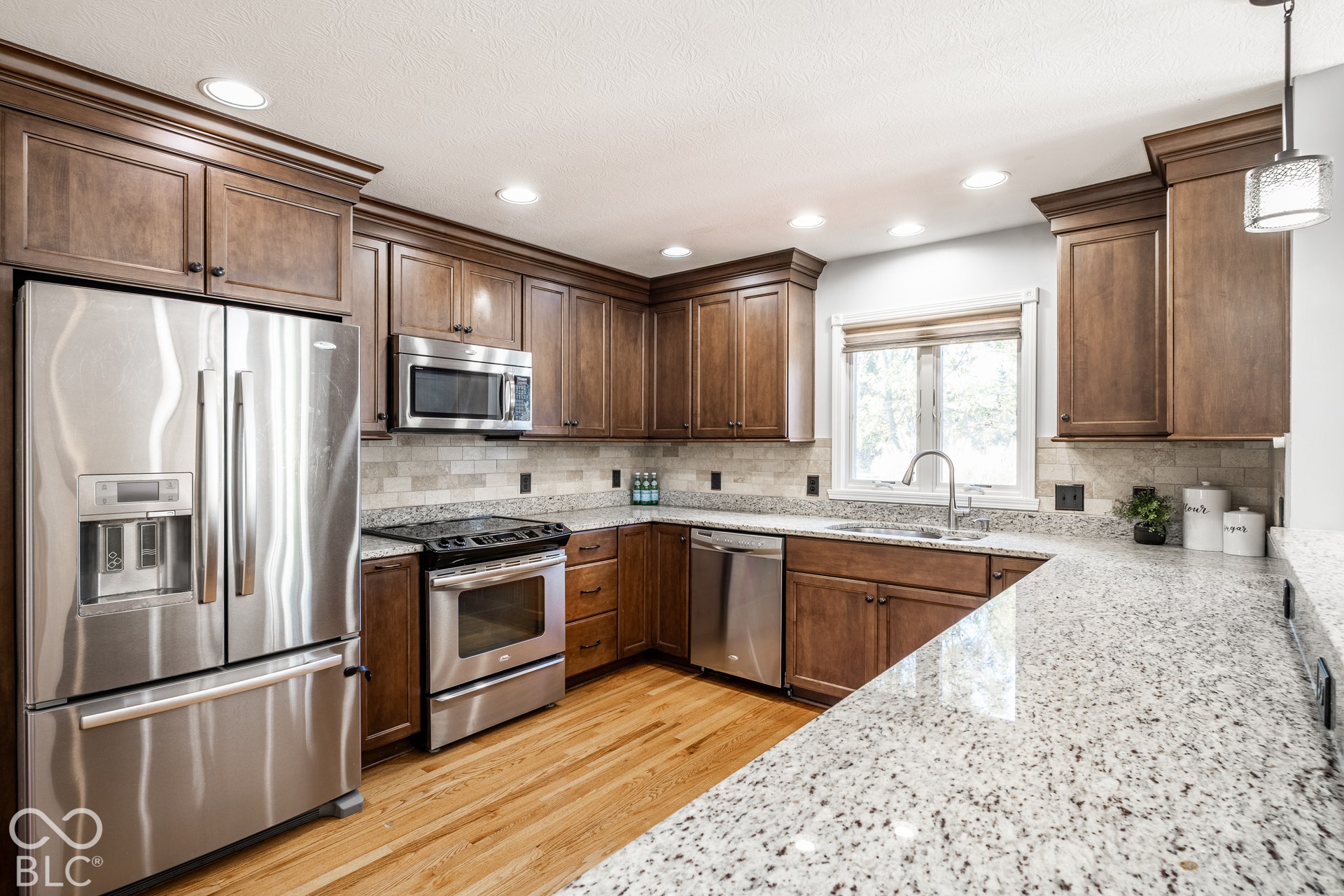 Kitchen featuring wood cabinetry, stainless steel appliances, stone countertops, a tile backsplash, and wood flooring