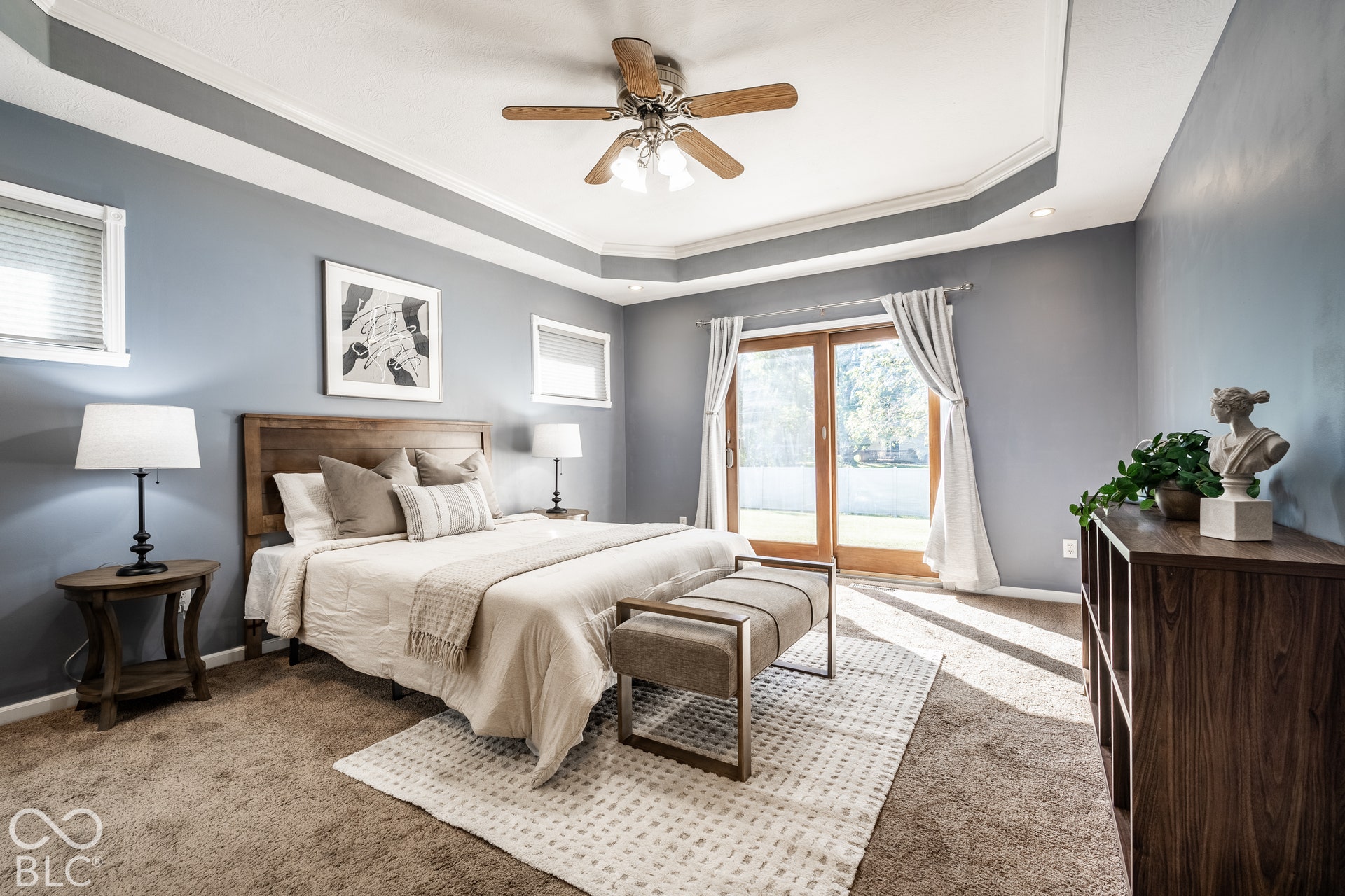 Primary suite bedroom with tray ceiling with crown molding, ceiling fan, doorway to private patio