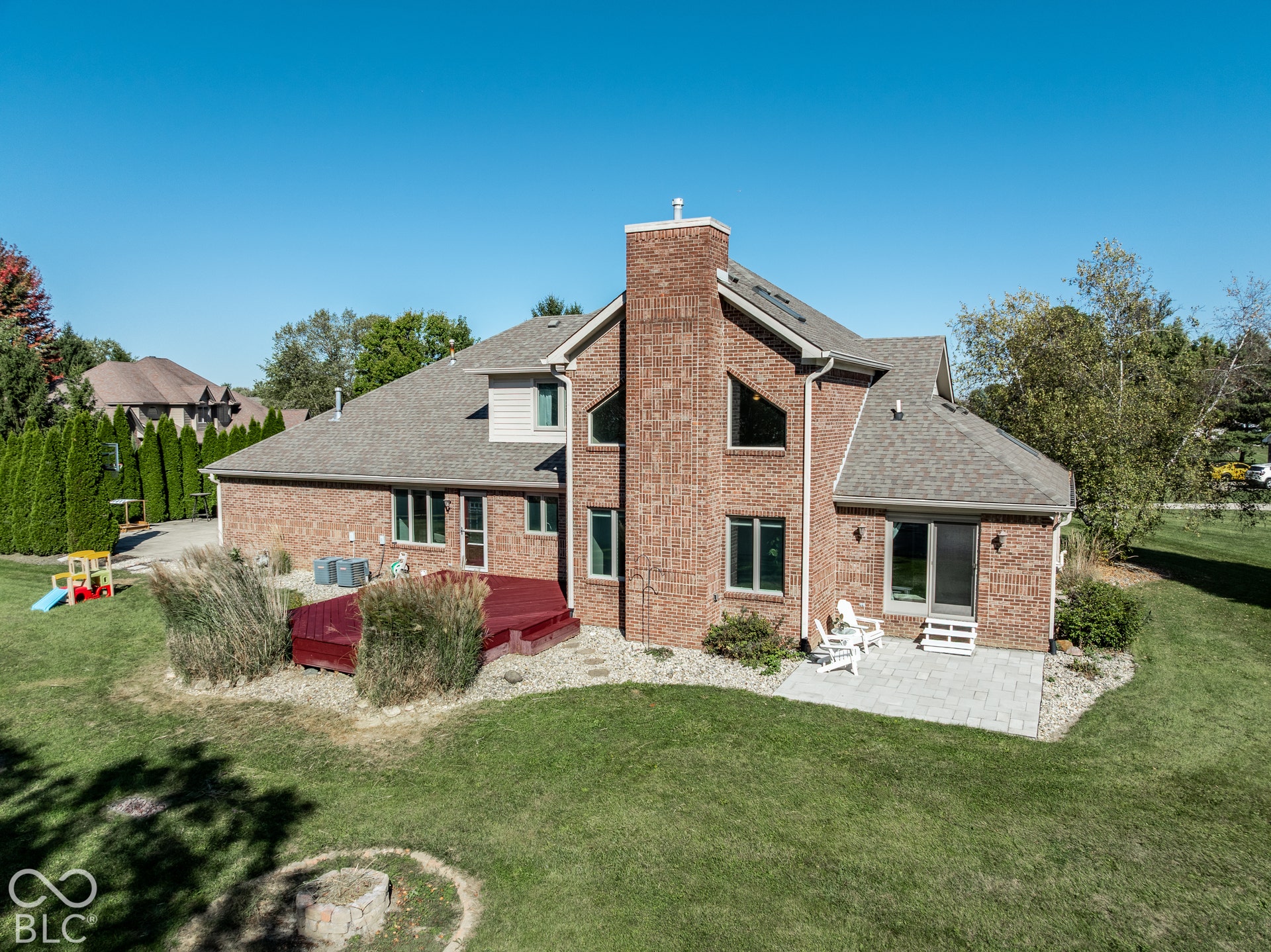 Brick exterior, deck, a paver patio, and lawn with fire pit area