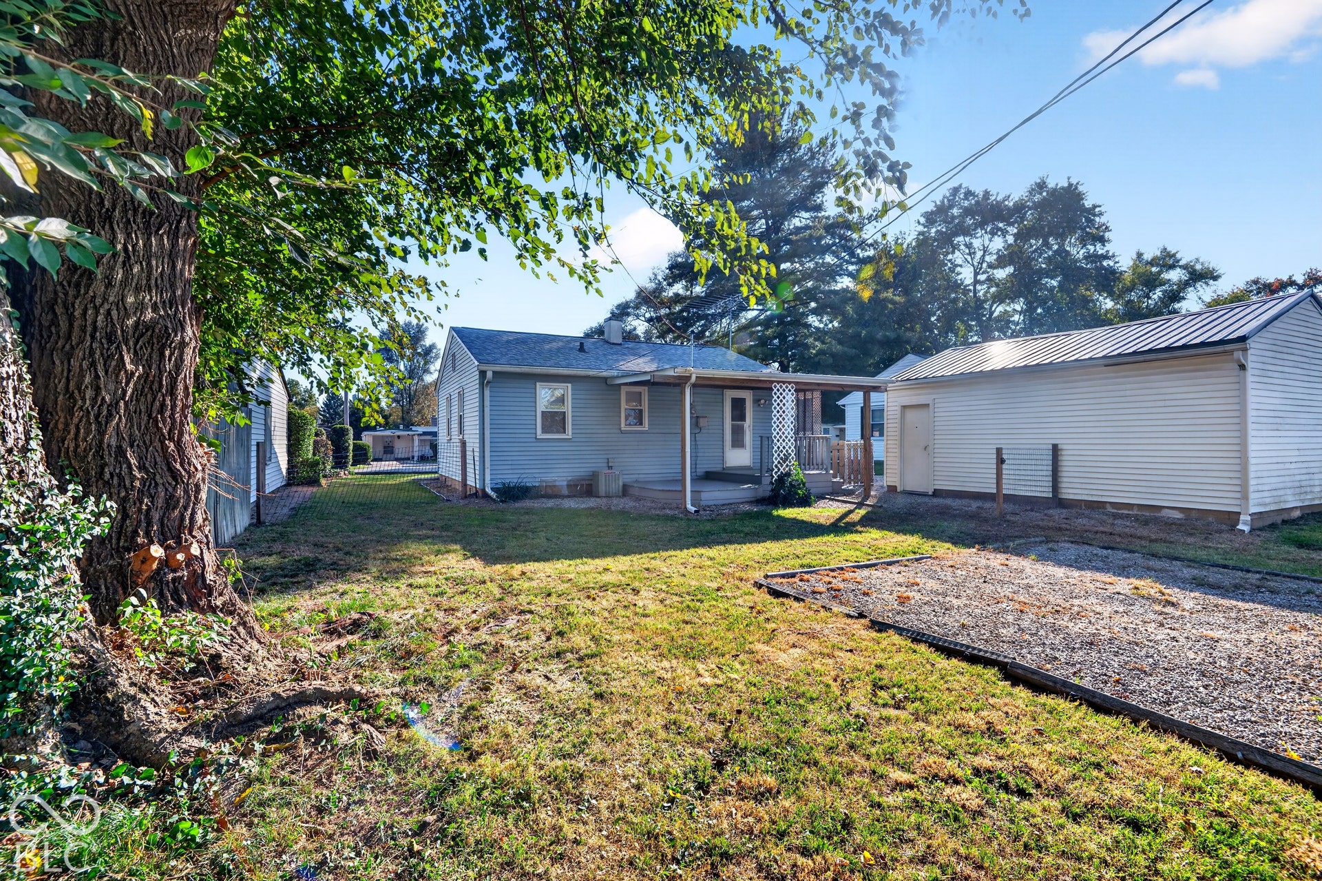 2706 13th Street, Columbus, IN 47201 Exterior grounds featuring a detached garage, covered rear patio, mature trees, and a gravel pad