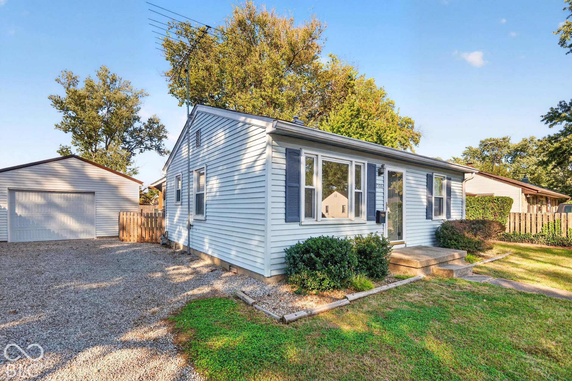 2706 13th Street, Columbus, IN 47201 Light-colored vinyl siding exterior with decorative shutters, concrete front steps, and a detached single-car garage featuring a gravel driveway