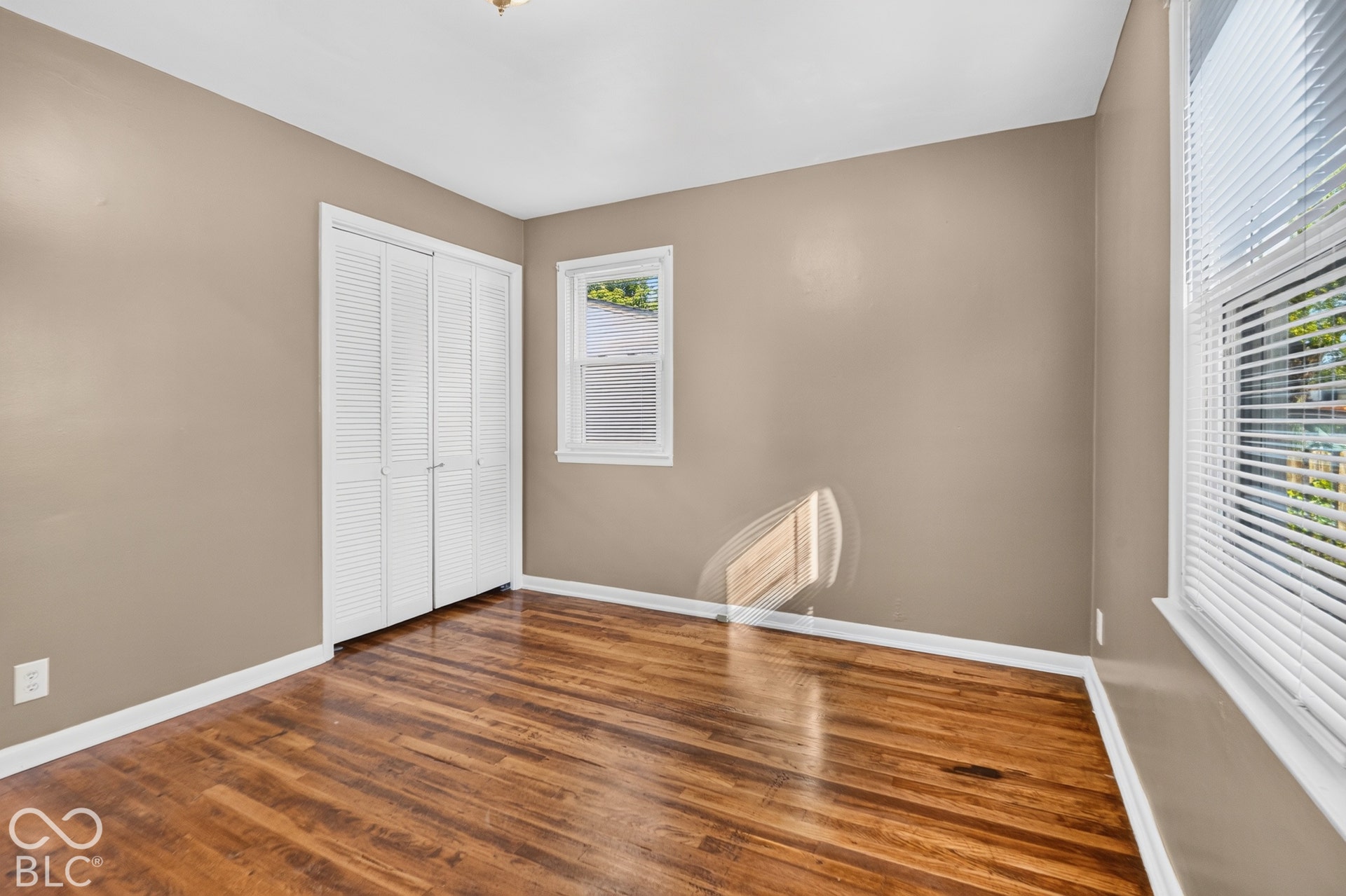2706 13th Street, Columbus, IN 47201 Room featuring wood-finish flooring, dual-panel louvered closet doors, and multi-pane windows with horizontal blinds