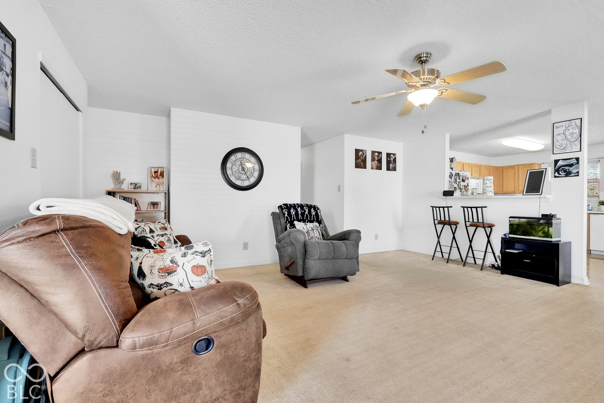 Open-concept living area featuring a ceiling fan with integrated lighting, carpeted flooring, and a breakfast bar with a tile counter