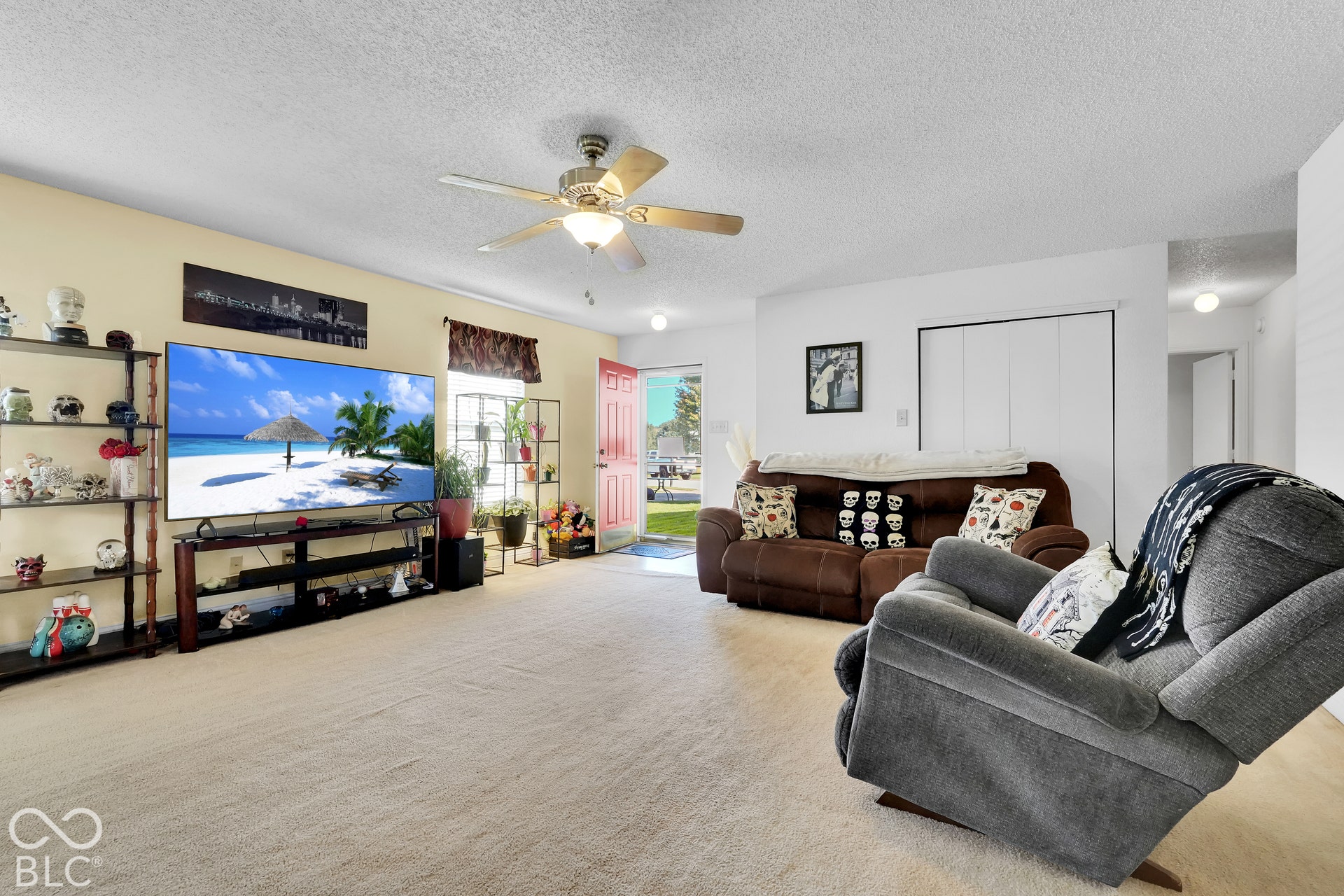 Textured carpeting, ceiling fan with integrated lighting, and a red entry door