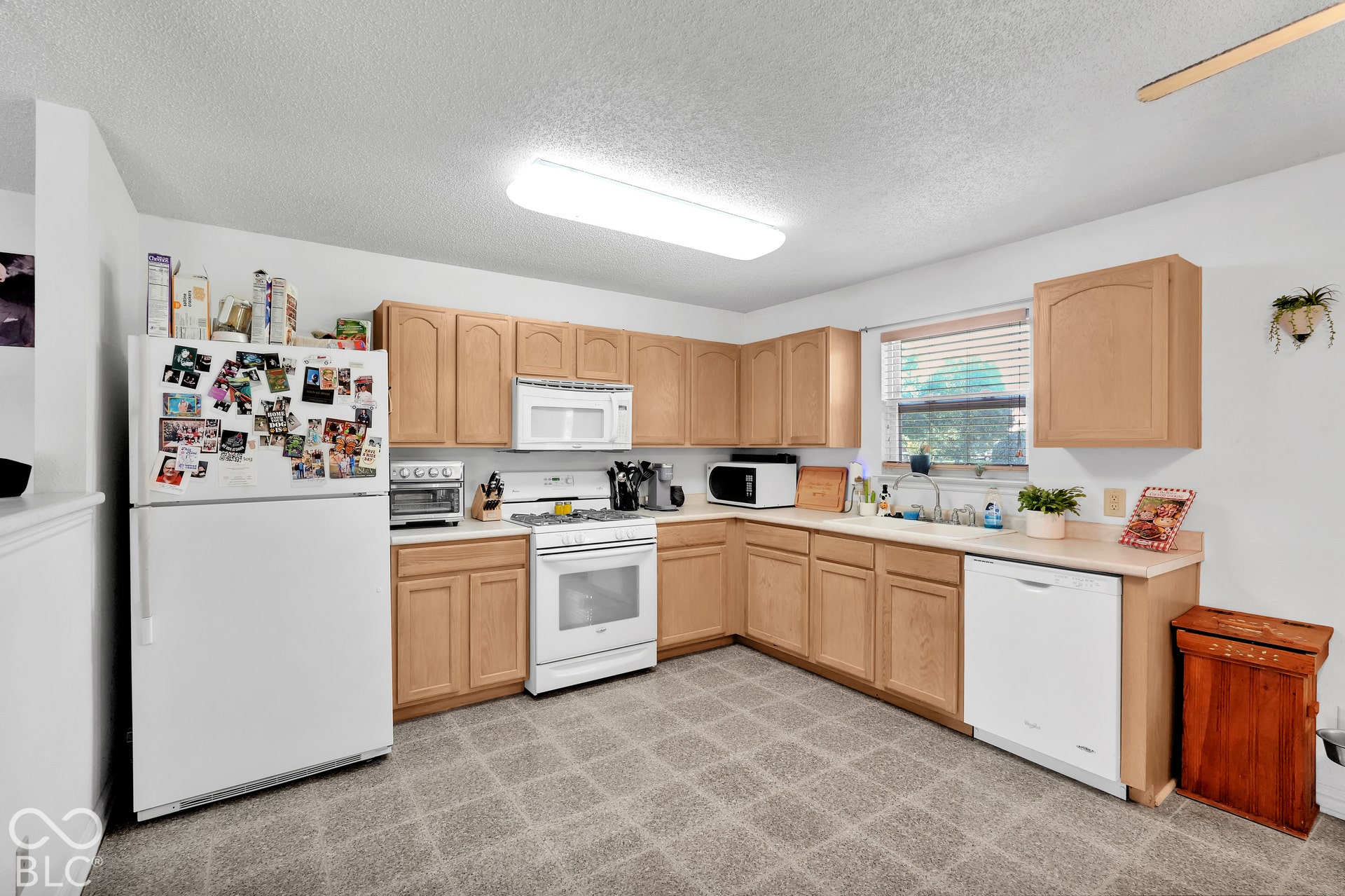 Kitchen featuring light wood-finish cabinetry, white appliances, L-shaped countertops, and a window