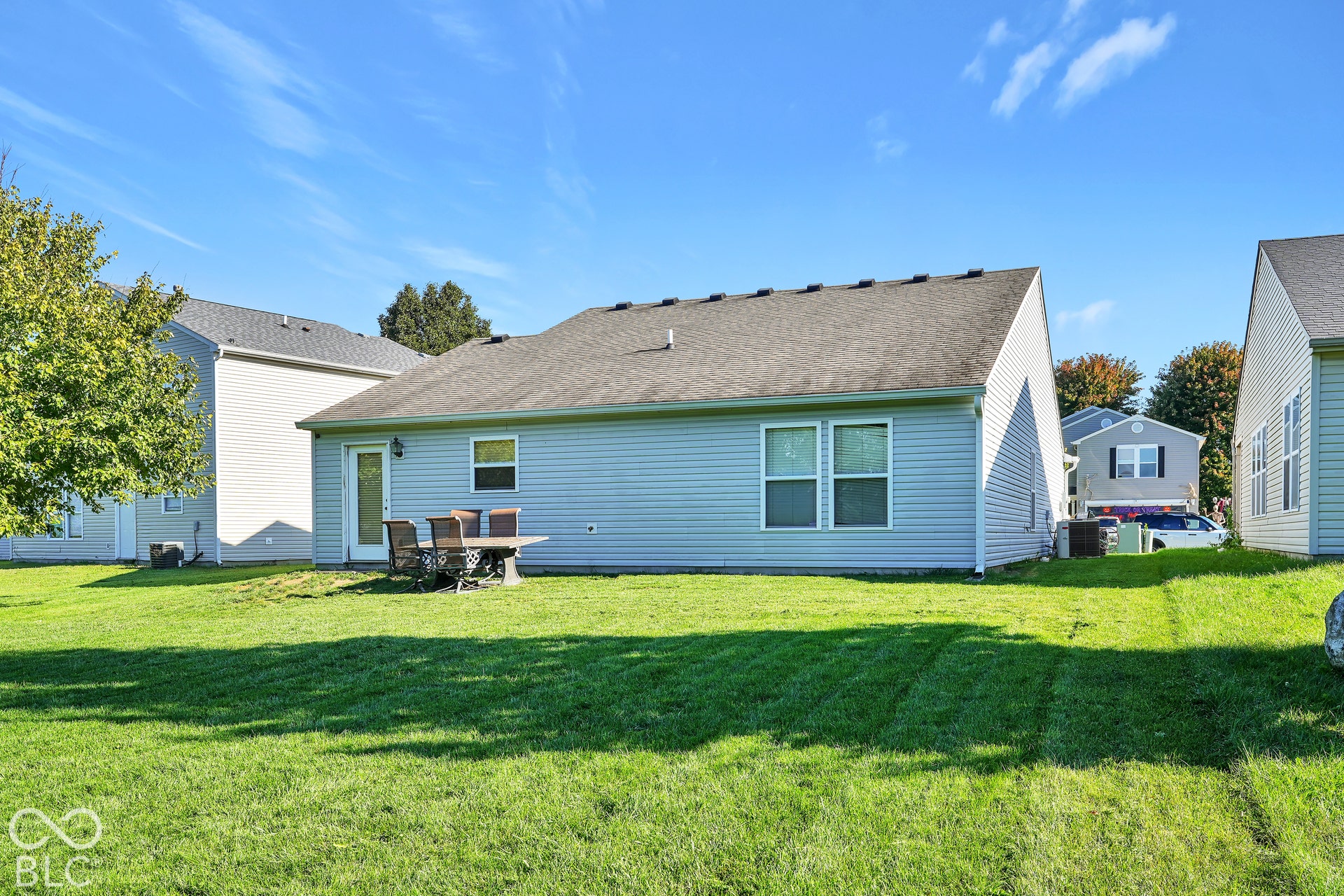 Expansive rear yard featuring green lawn, light blue horizontal siding, and a back door with a window