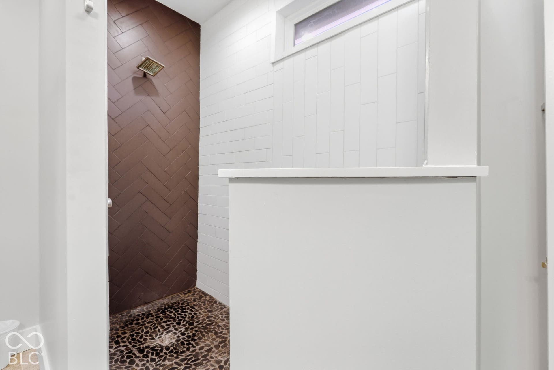 Walk-in shower featuring a dark herringbone tile accent wall, pebble floor, and a rectangular window