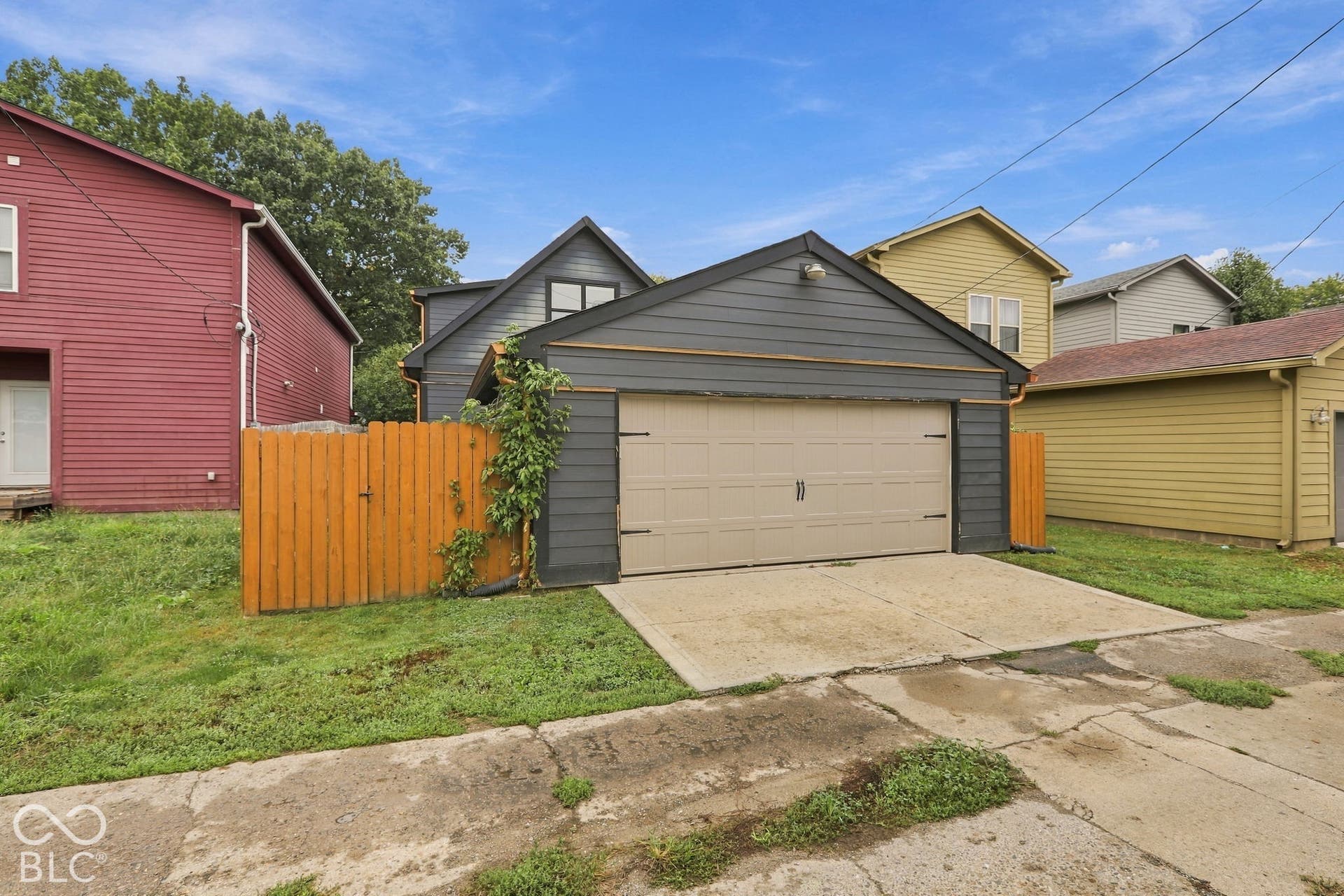 Detached garage with a light-colored garage door and dark siding, concrete driveway, and wooden fencing